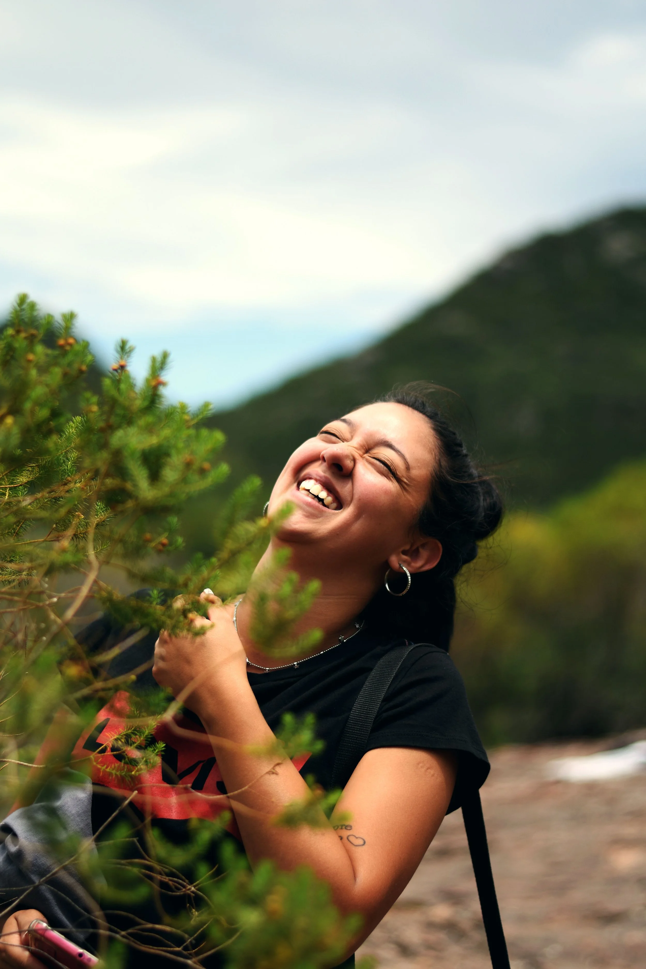 A woman in her 40s laughs as she stands by a bush in nature