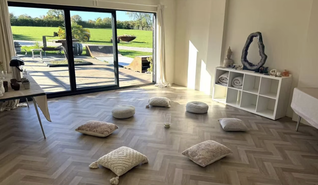 Living room with floor cushions arranged in a circle, large sliding glass door leading to a backyard with green grass, outdoor furniture, and trees.