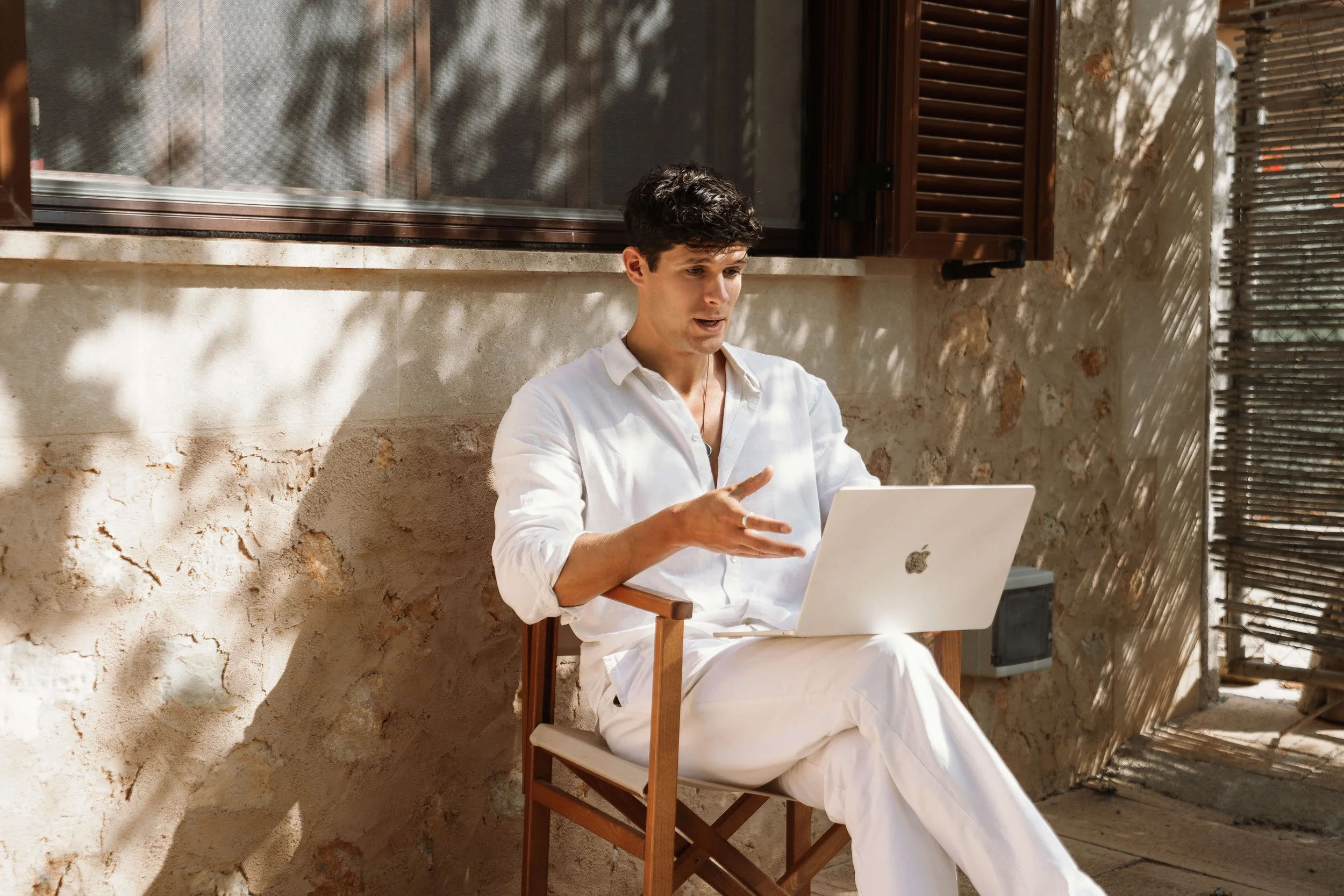 Man in white sitting outdoors working on a laptop