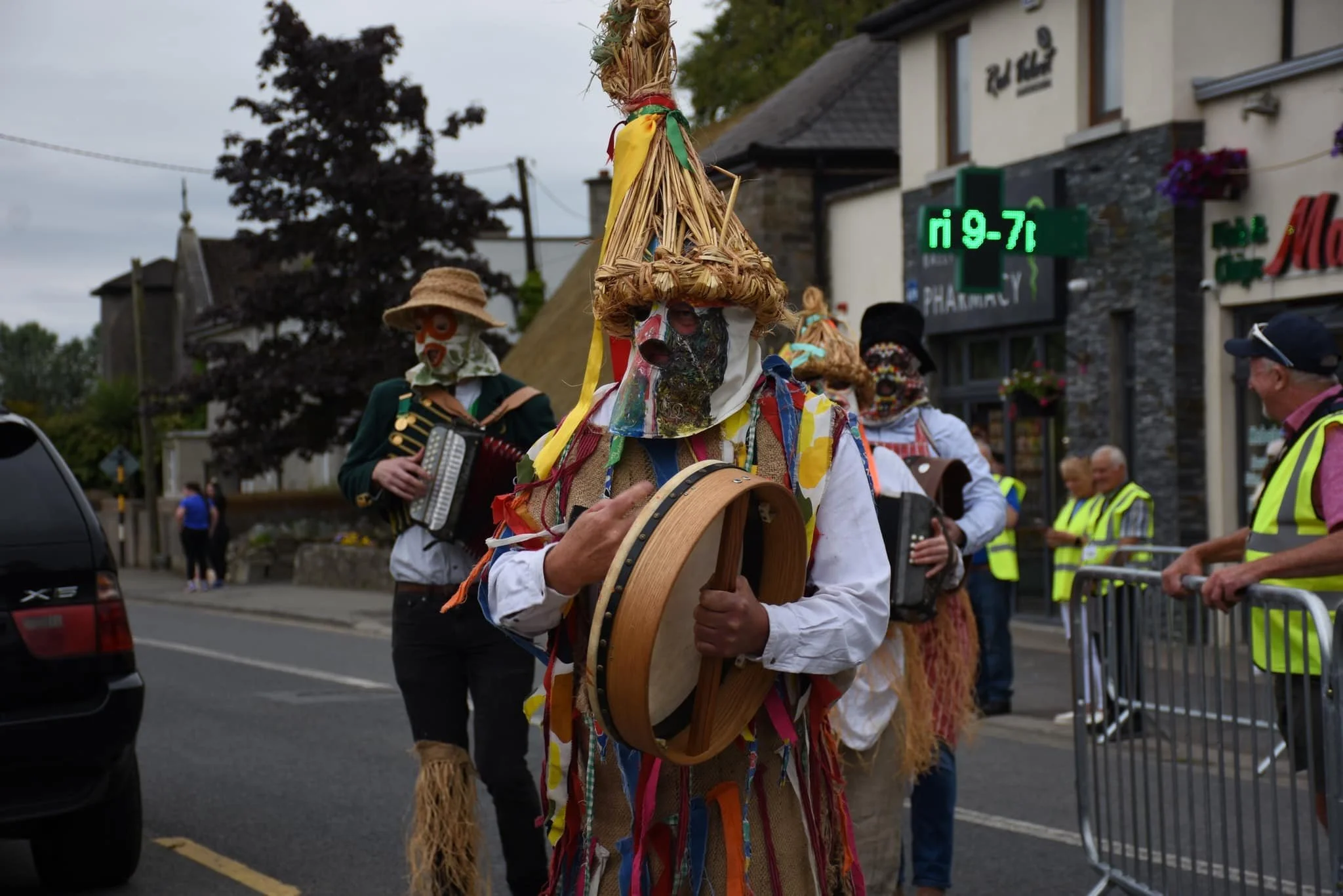 People dressed in traditional costumes with masks, playing musical instruments during a street parade or festival.