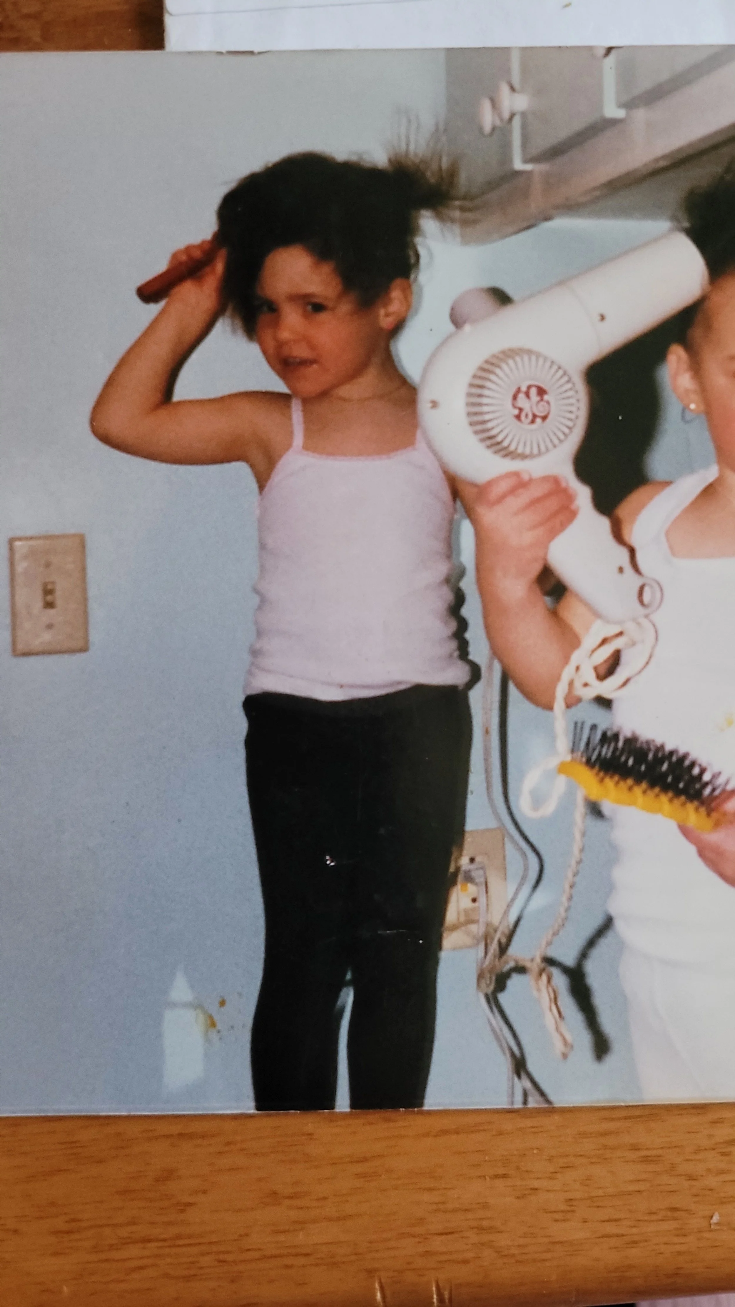 Dès mon plus jeune âge, ma passion pour la coiffure était déjà bien présente. Sur cette photo, je m'amuse à coiffer mes cheveux, une activité qui annonçait déjà mon avenir dans le monde de la coiffure holistique et des soins capillaires naturels.