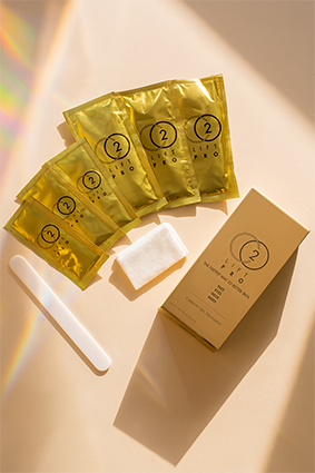 Five packets of CO2Lift Pro, a white spatula, a white applicator pad, and a beige box with a similar design and the number '2' on it, placed on a white surface with sunlight and shadows.
