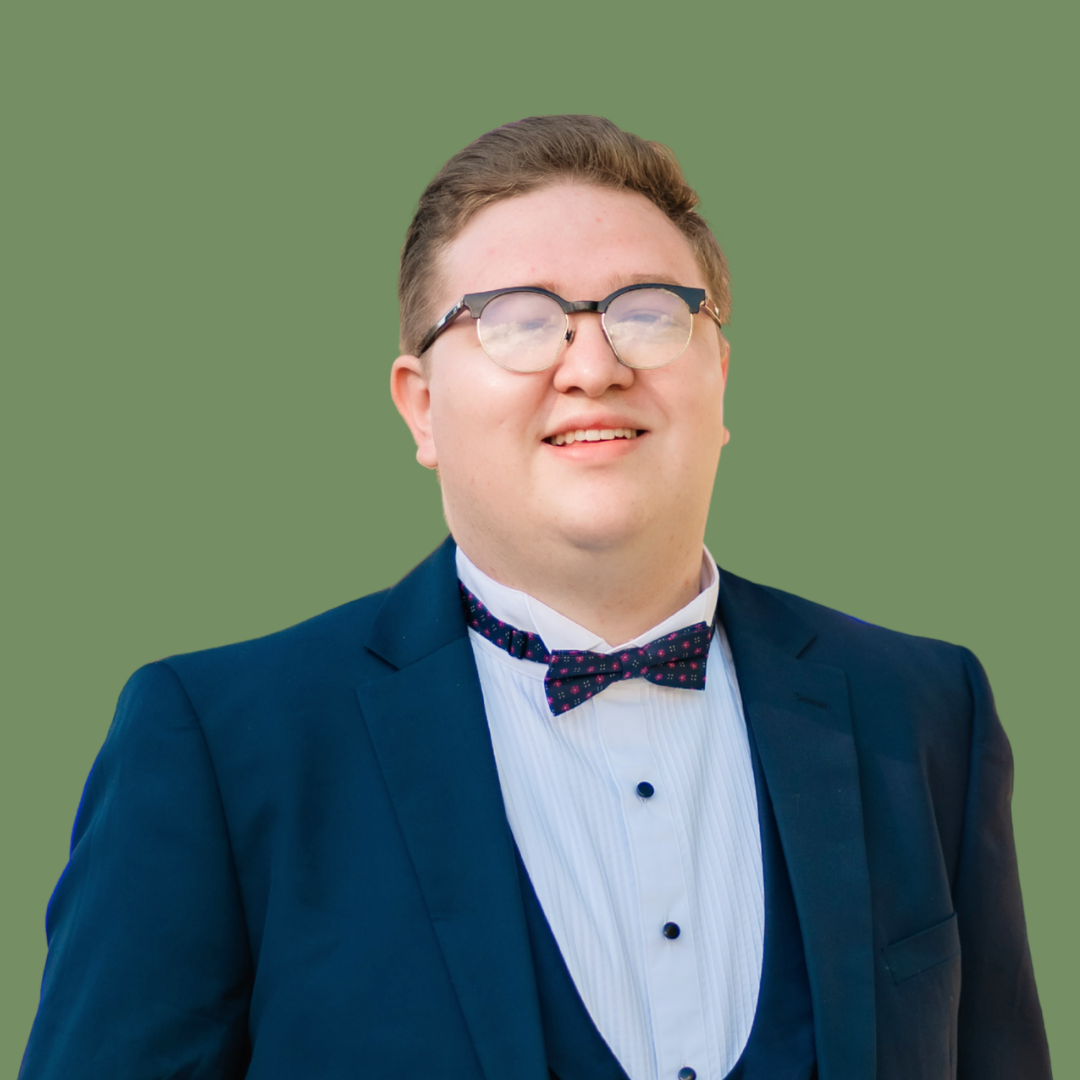 Portrait of a young man wearing glasses, a tuxedo, white dress shirt, and bow tie, smiling with a green background.