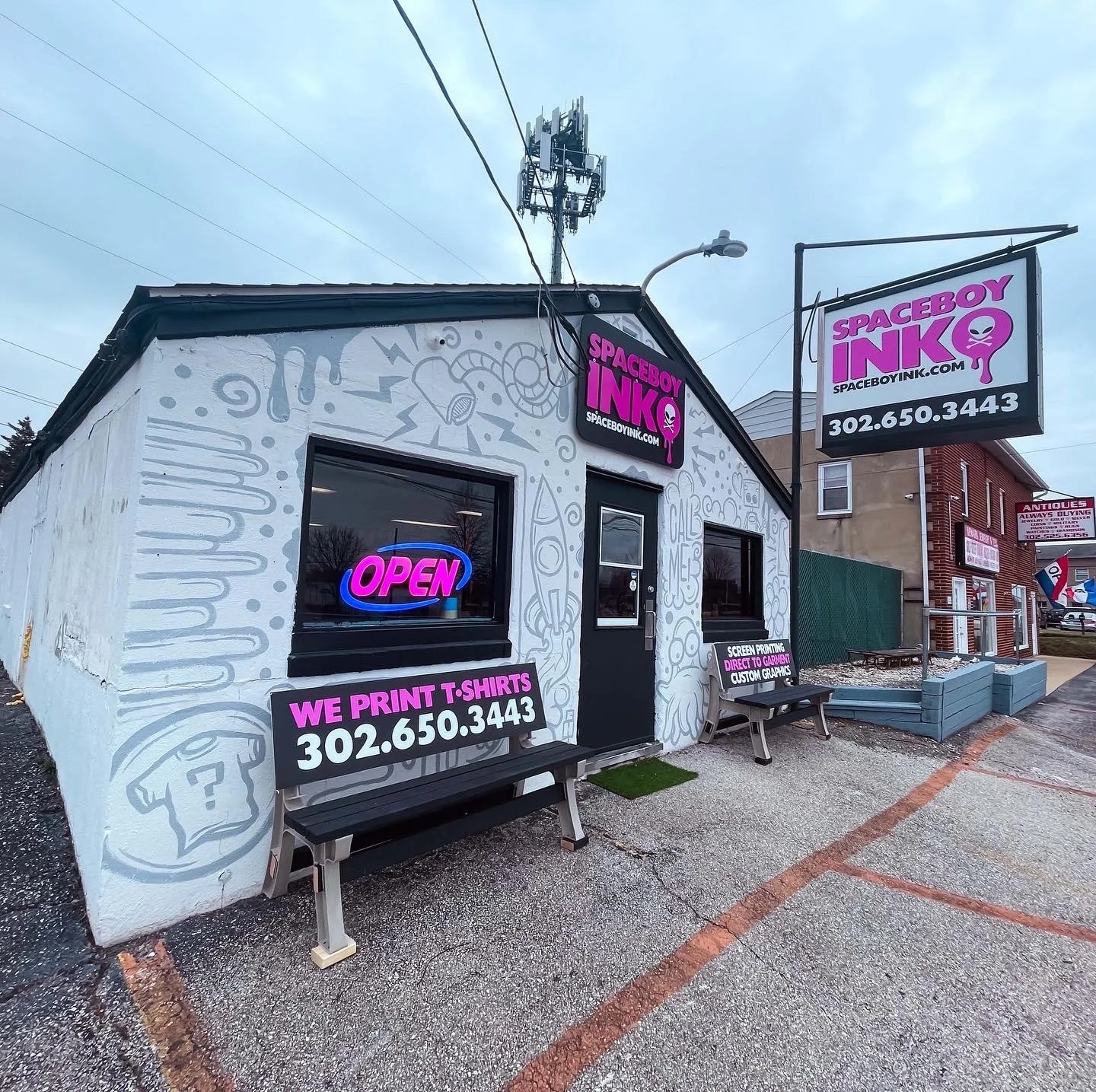 Exterior of Spaceboy Ink shop with graffiti art, neon signs, and advertisement for T-shirt printing.