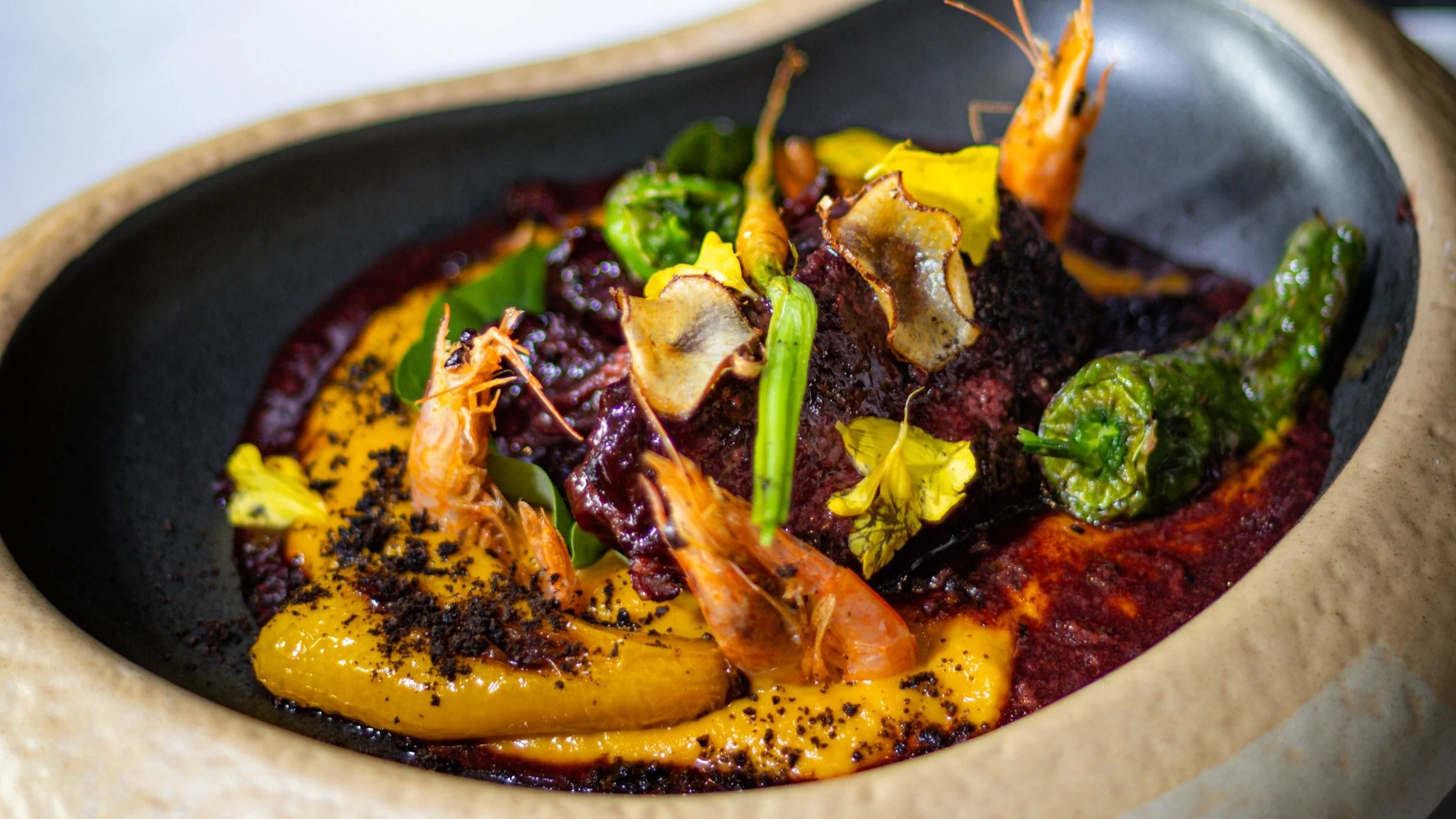 Plato de carne con mariscos, salsa y vegetales decorativos, servido en una cazuela de barro.