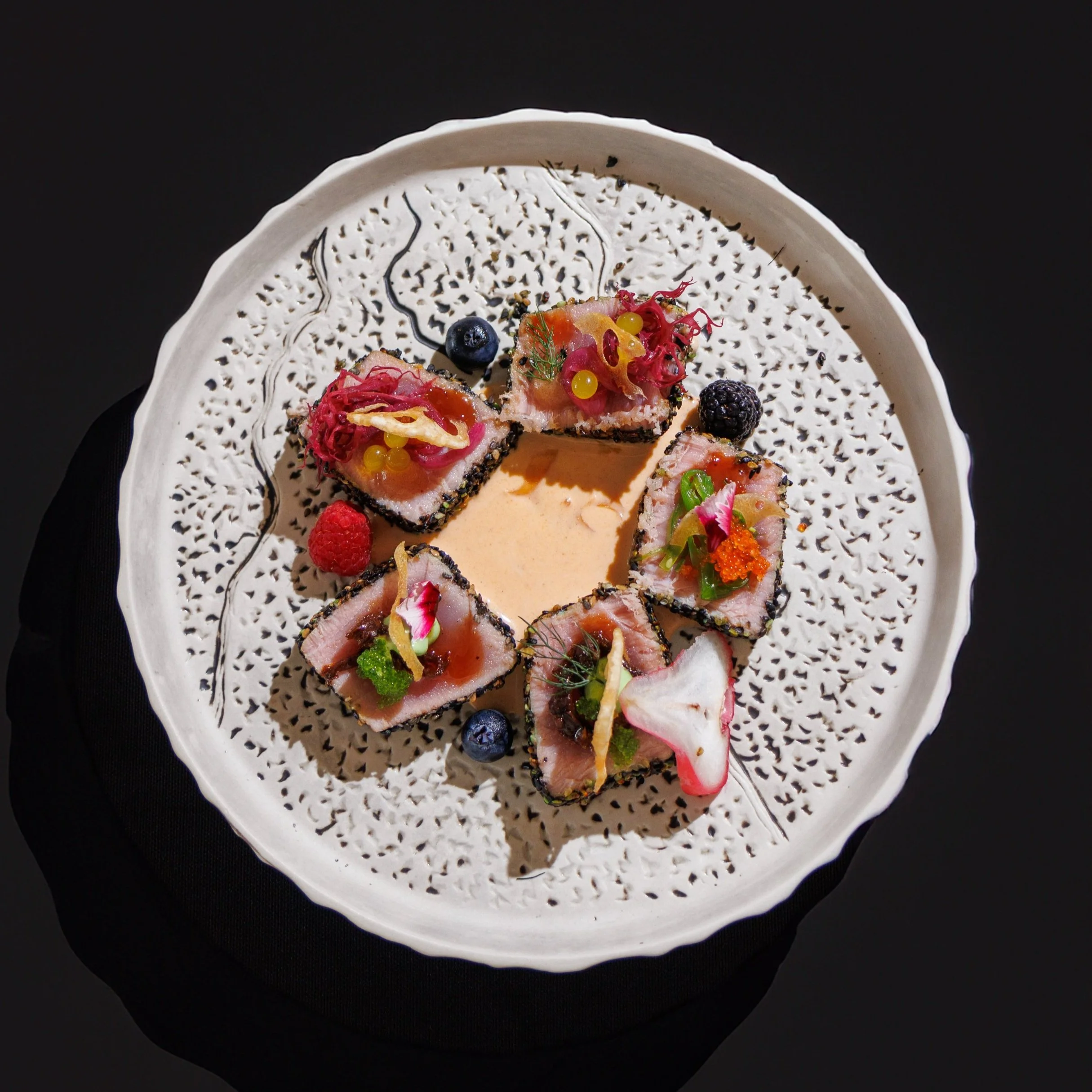 Tartar de atún con frutas y decoraciones en un plato blanco decorado con motivos negros.