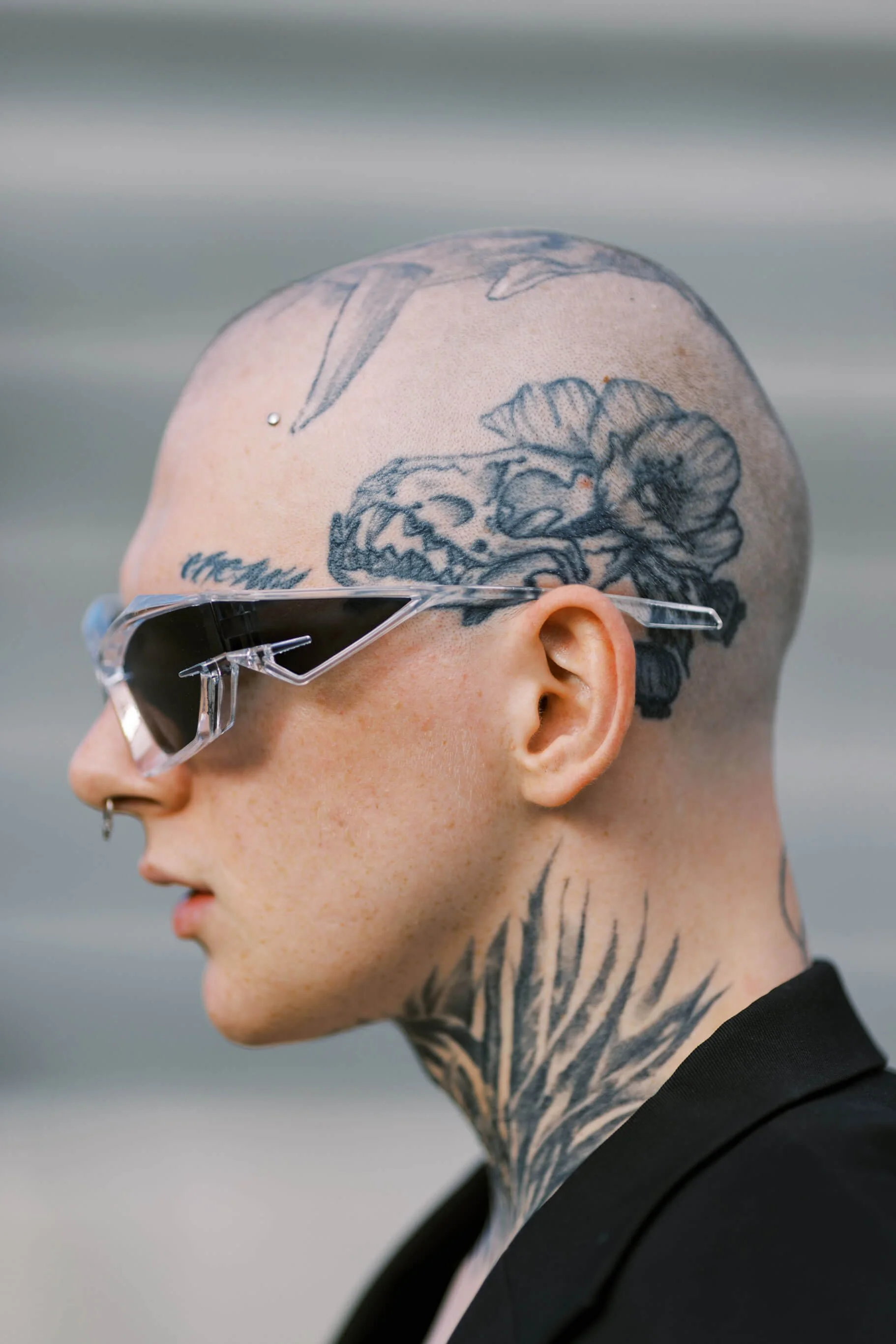 Ragazza con tatuaggi sulla testa e sul collo, occhiali da sole trasparenti, cappello di capelli rasati
