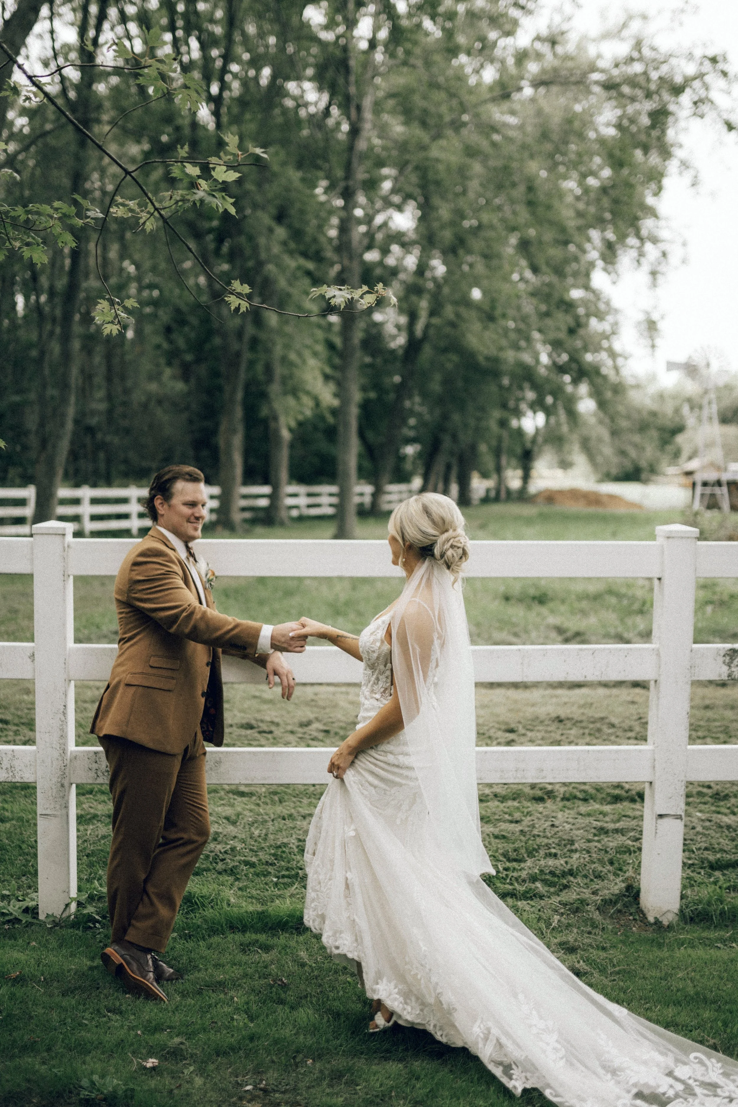 A bride and groom holding hands in front of a white fence outdoors with trees in Chiliwack, BC.