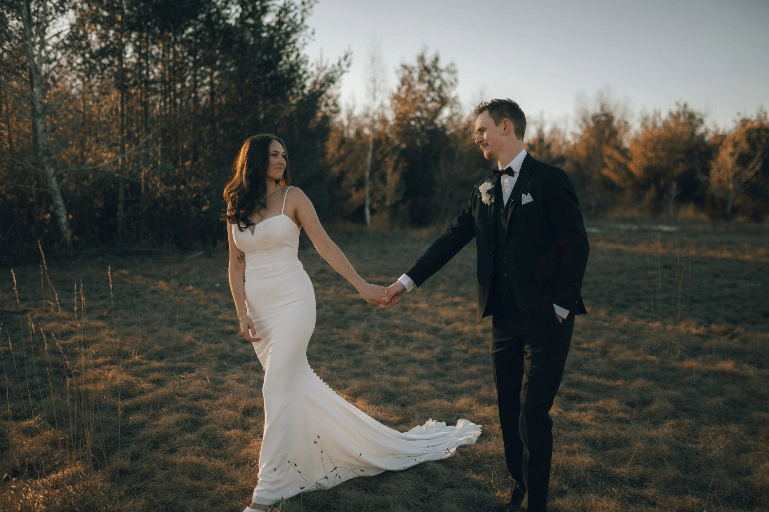Bride and groom holding hands in a field during sunset.