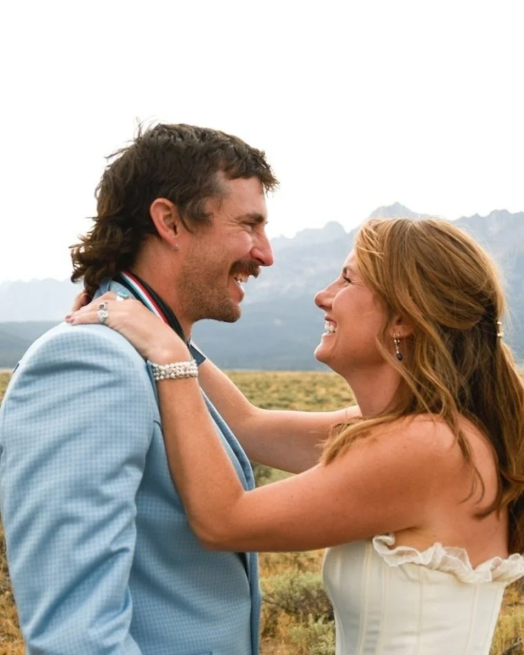 A happy couple smiling and embracing outdoors with mountains in the background.