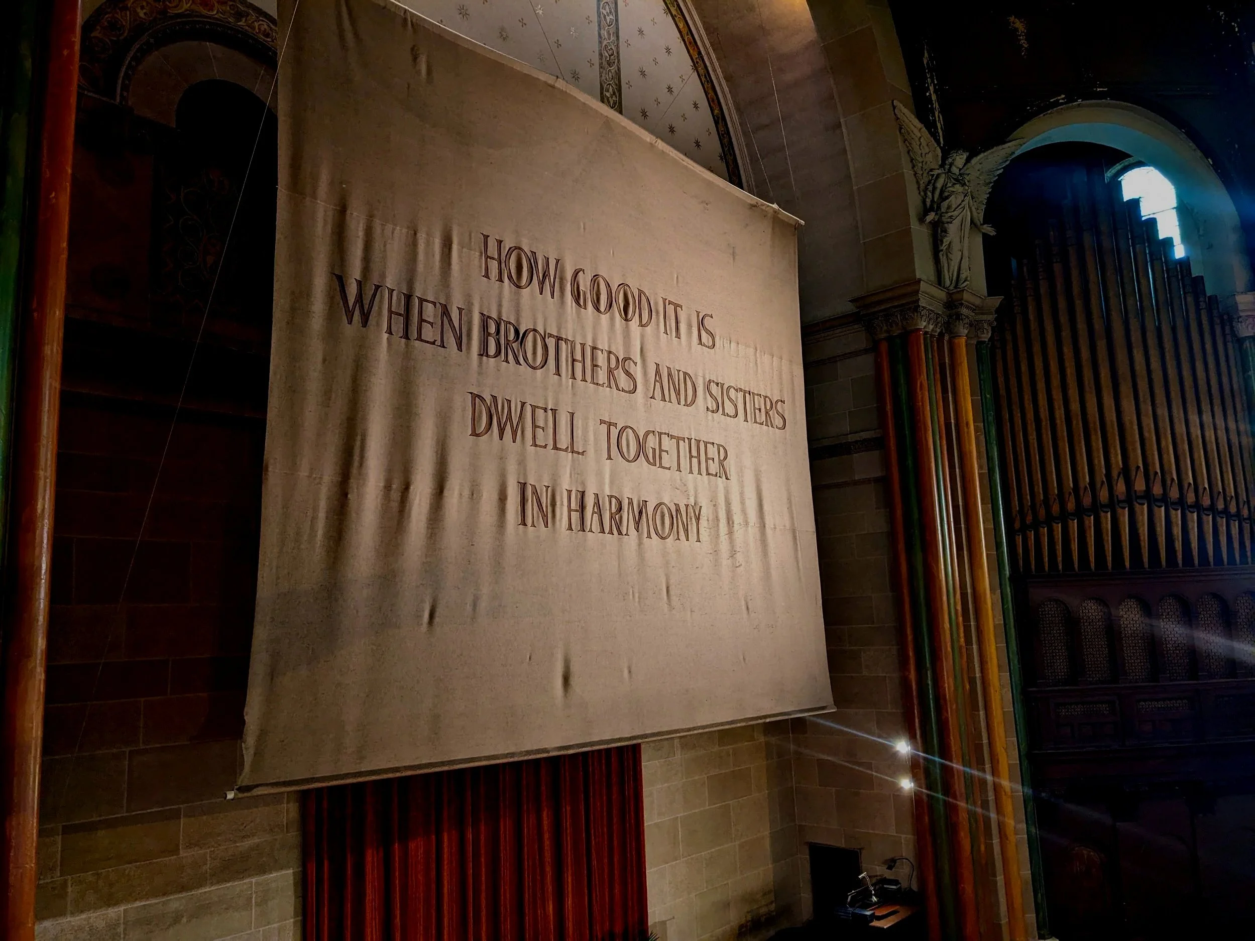 A large fabric banner inside a church with the quote: "How good it is when brothers and sisters dwell together in harmony."