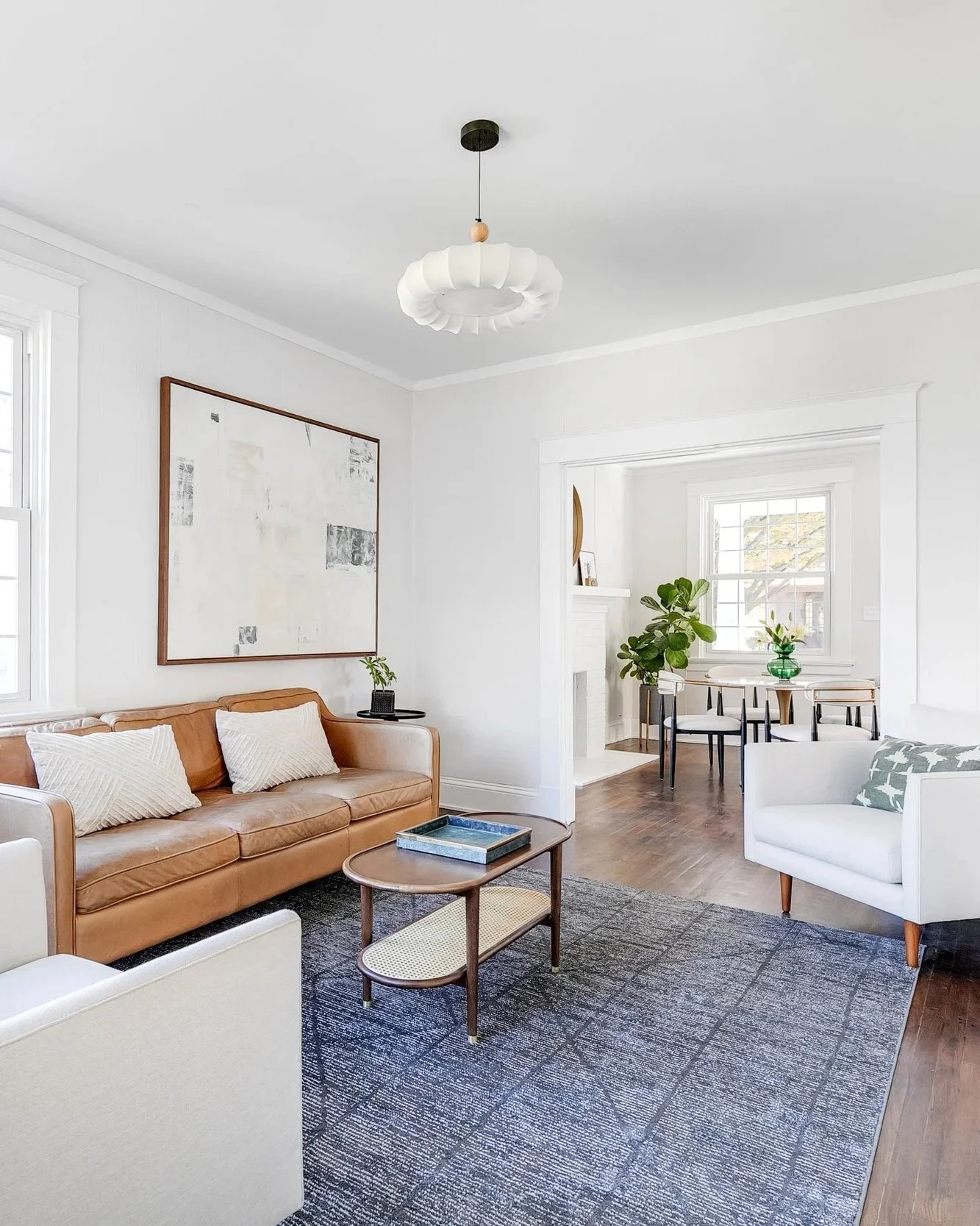 Custom living room design from Designs Delivered featuring a brown leather sofa, two white armchairs, brass pendant lights, and a large abstract artwork, showcasing the personalized results available in the design customization service.