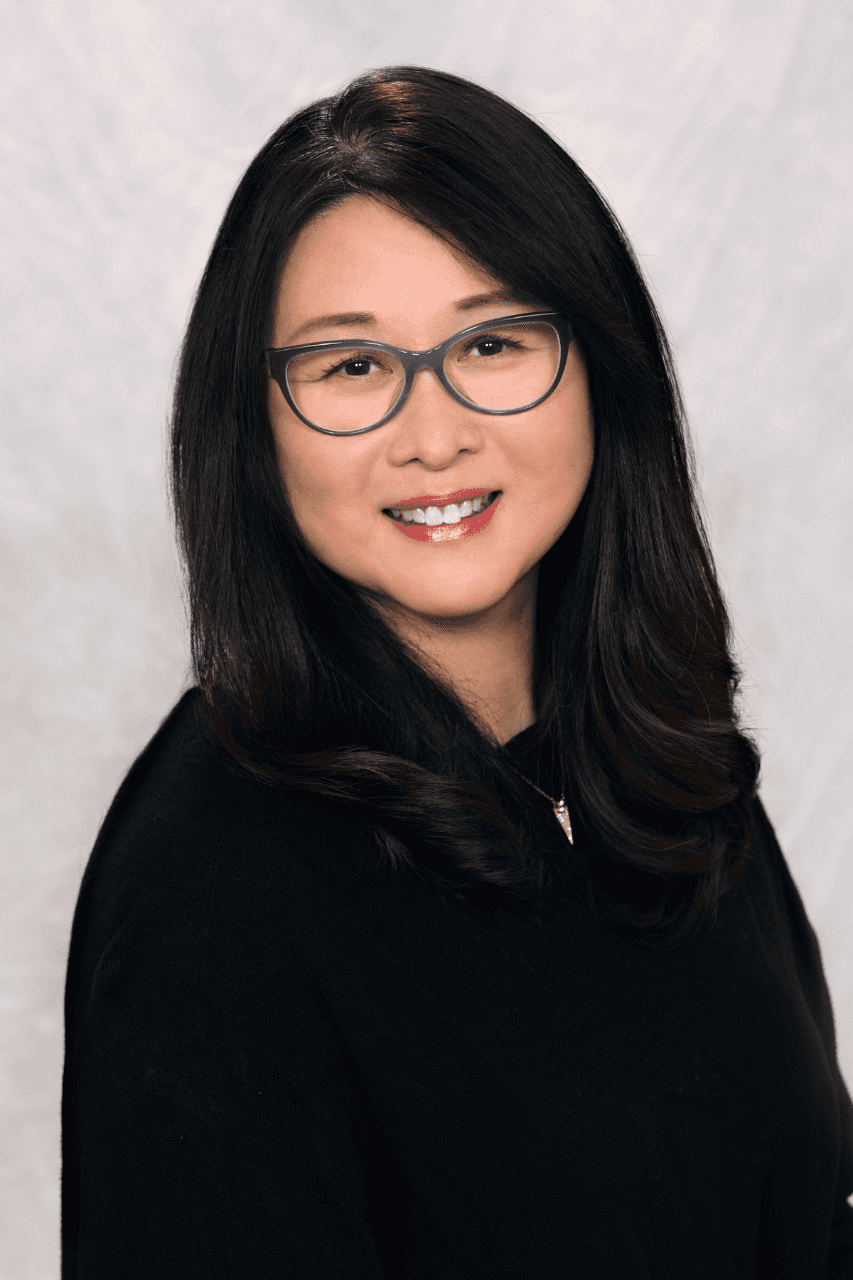 Person with long dark hair and glasses smiling against a light background.