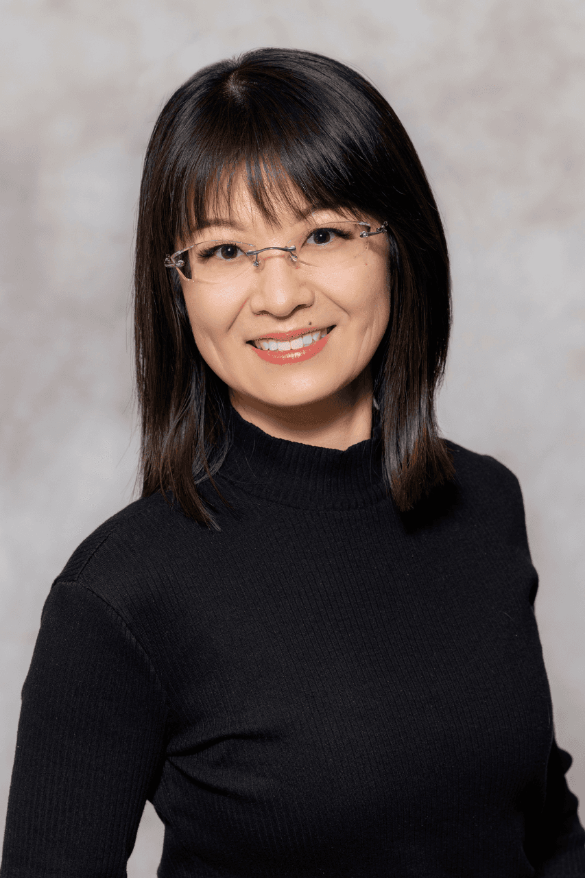Person wearing glasses and a black shirt, smiling at the camera with a neutral background.