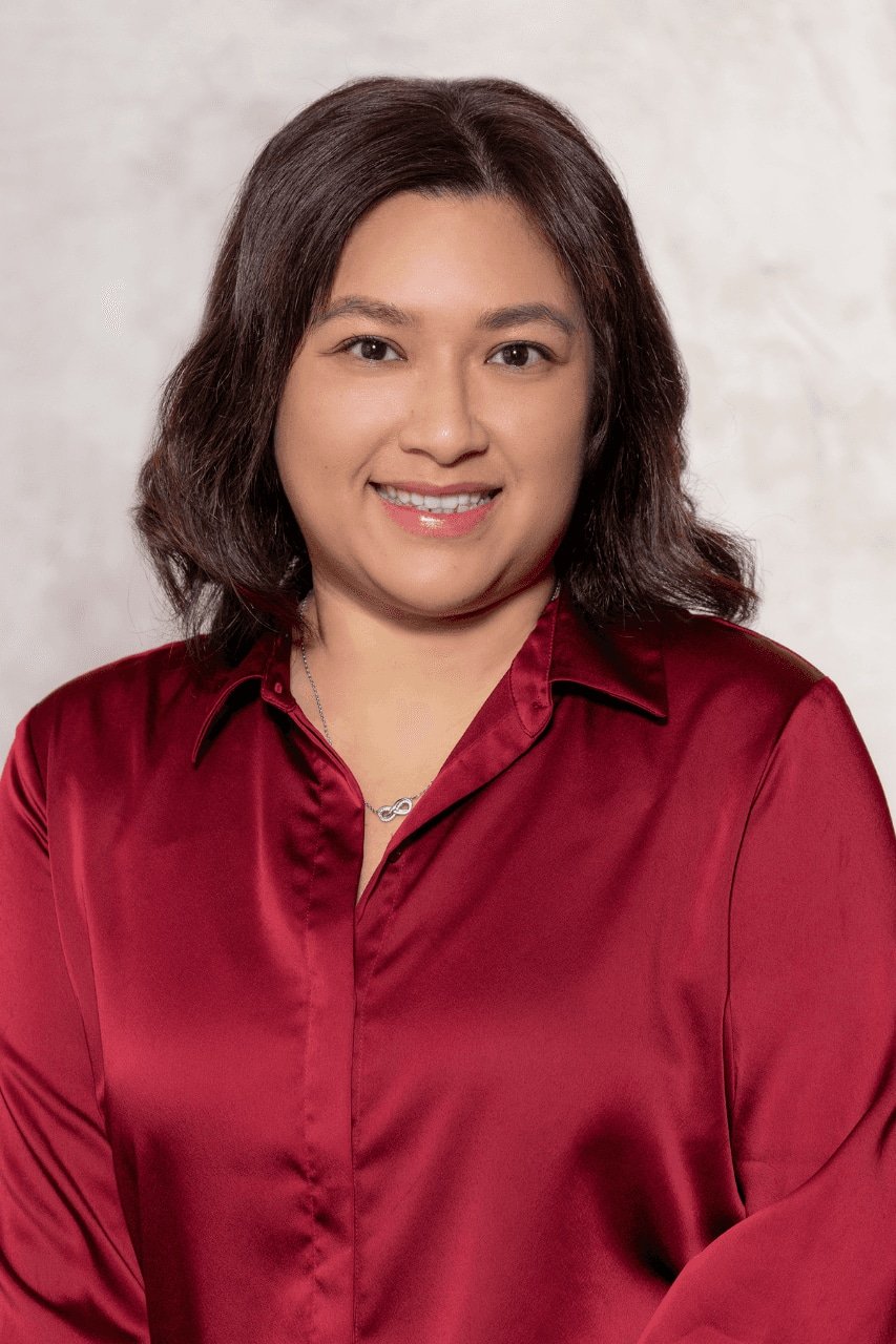 Woman wearing a red blouse, smiling at the camera with a light background.