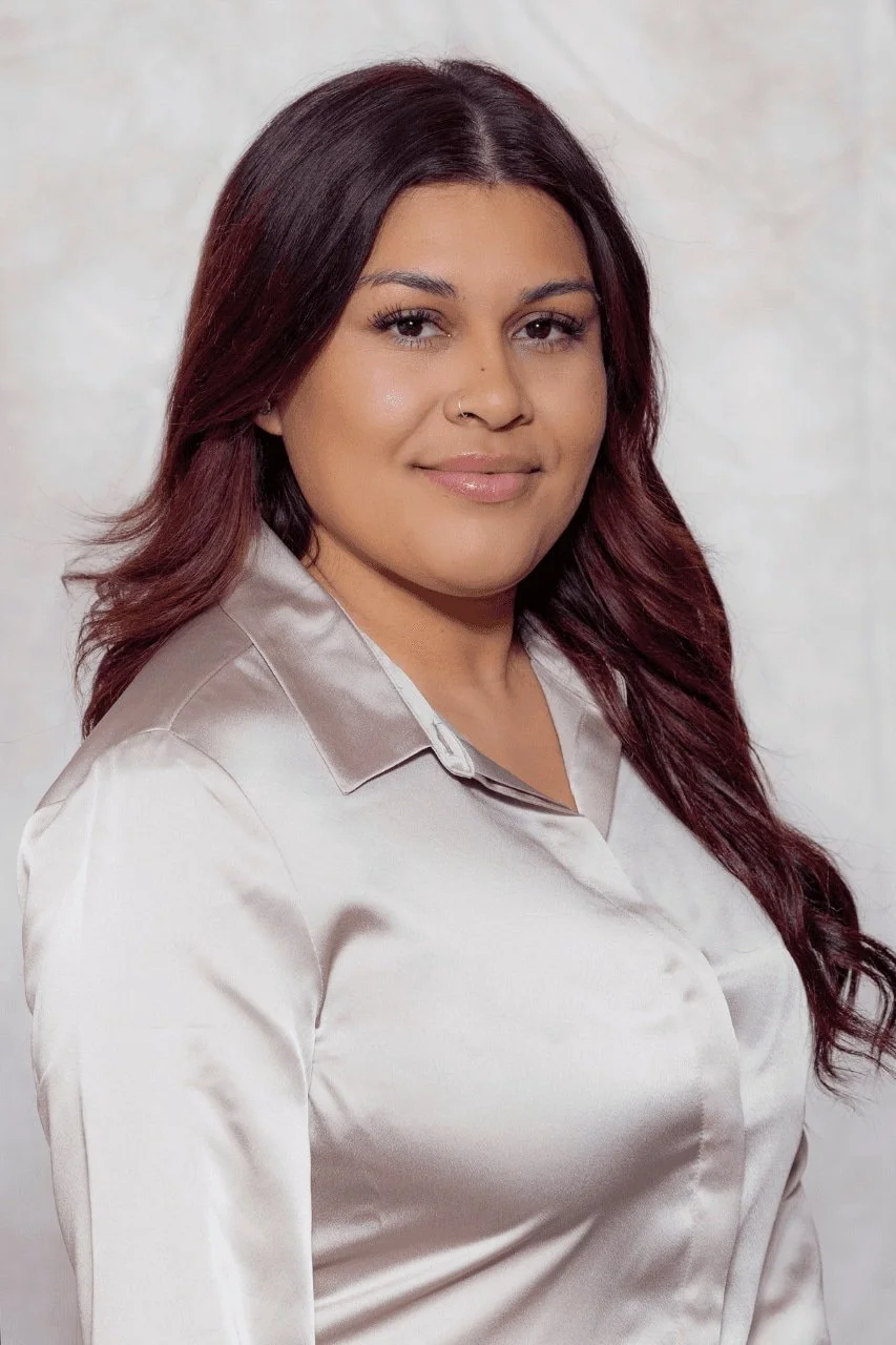 Smiling woman with long dark hair wearing a light-colored blouse.