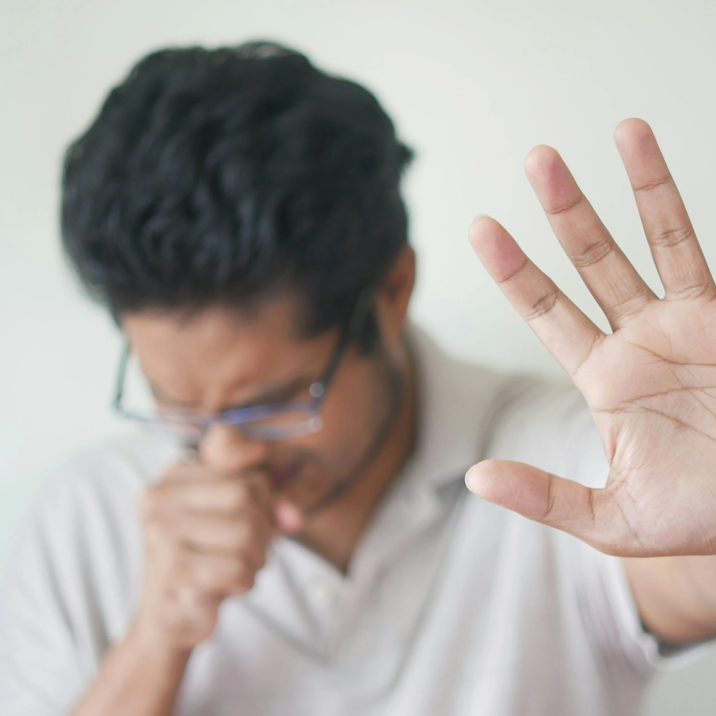 Man coughing into his fist with his other hand raised