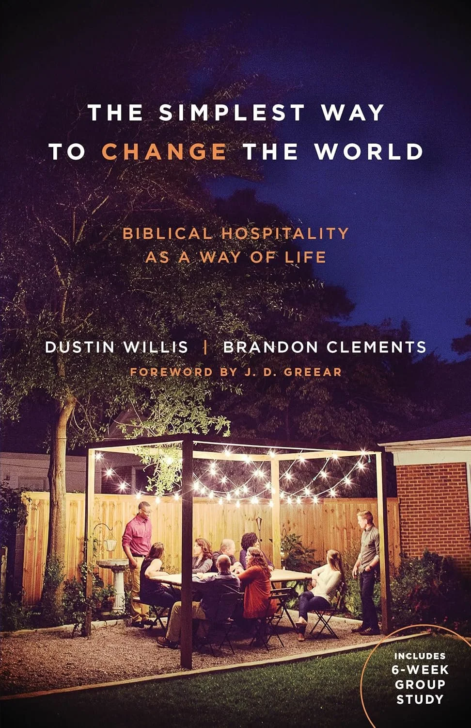 Book cover titled 'The Simplest Way to Change the World' with subtitle 'Biblical Hospitality as a Way of Life' by Dustin Willis and Brandon Clements, foreword by J. D. Grear. The background image shows a group of people gathered outdoors under string lights, sitting around a table, in a backyard setting at night.