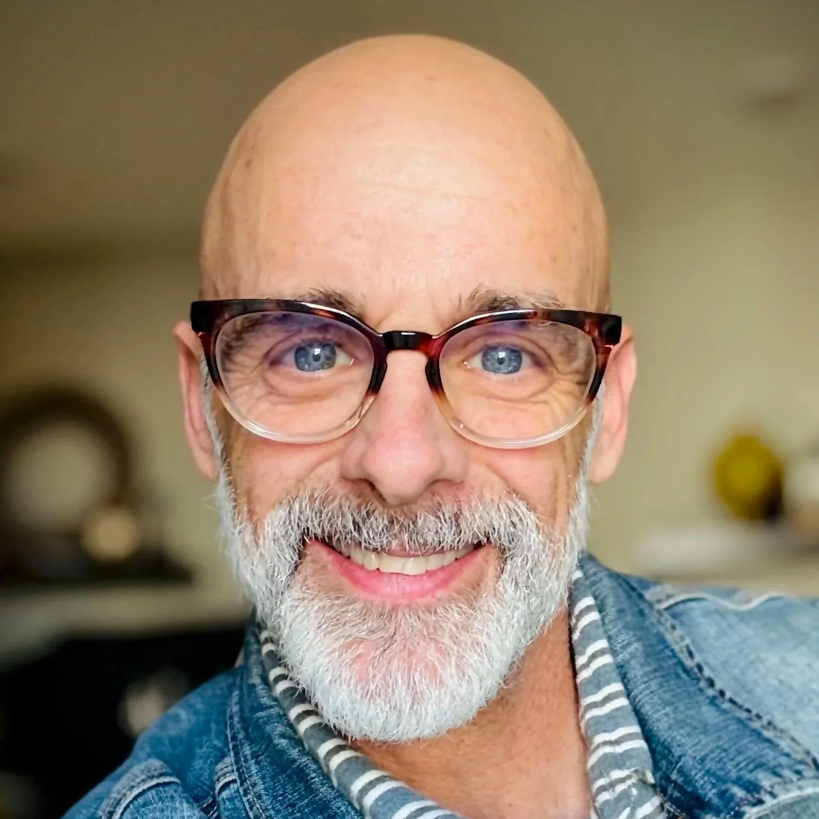 Close-up of a smiling middle-aged man with a bald head, gray beard, and glasses with tortoiseshell frames.