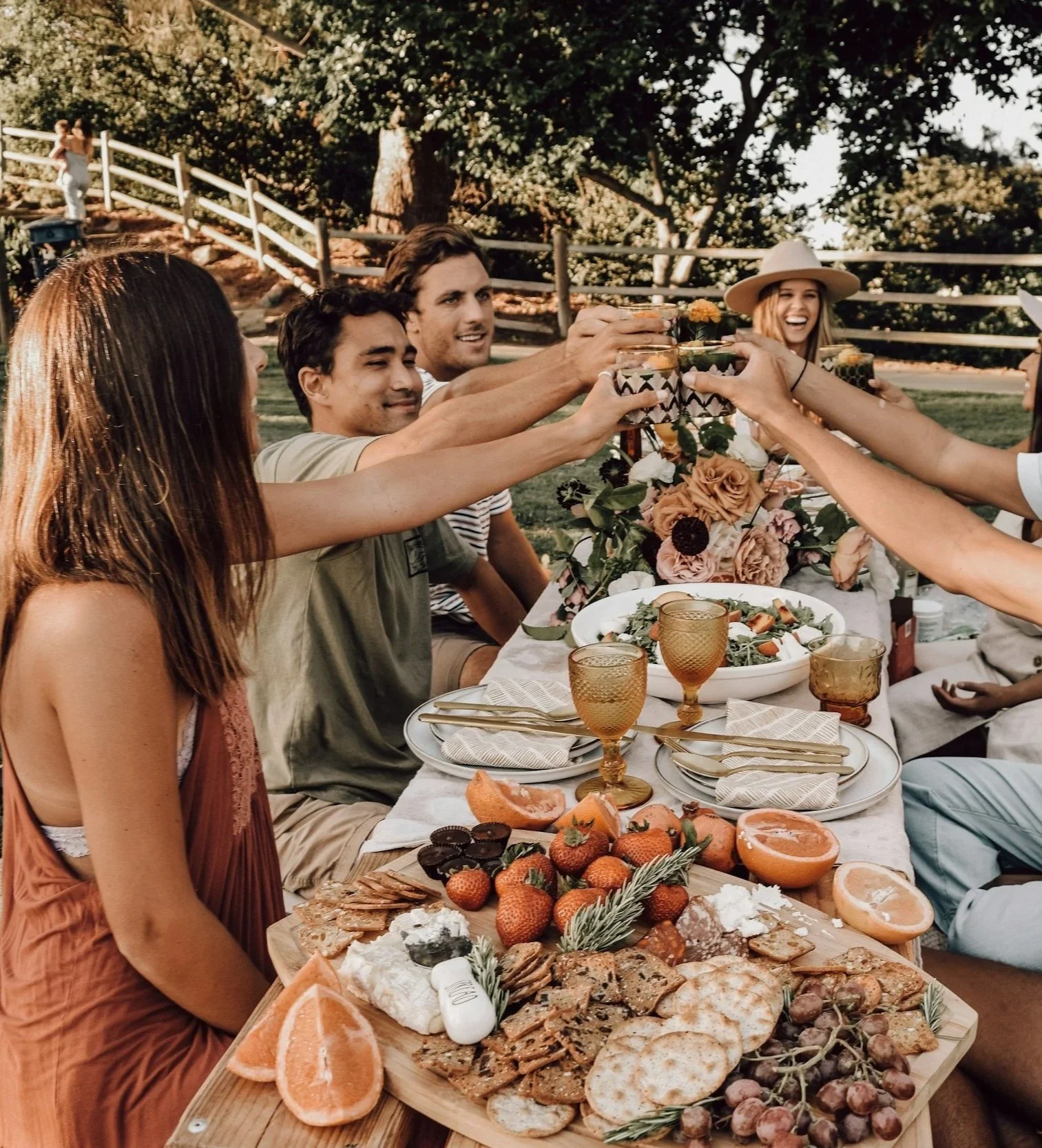 Group of friends gathered around an outdoor dining table sharing food and raising their glasses.