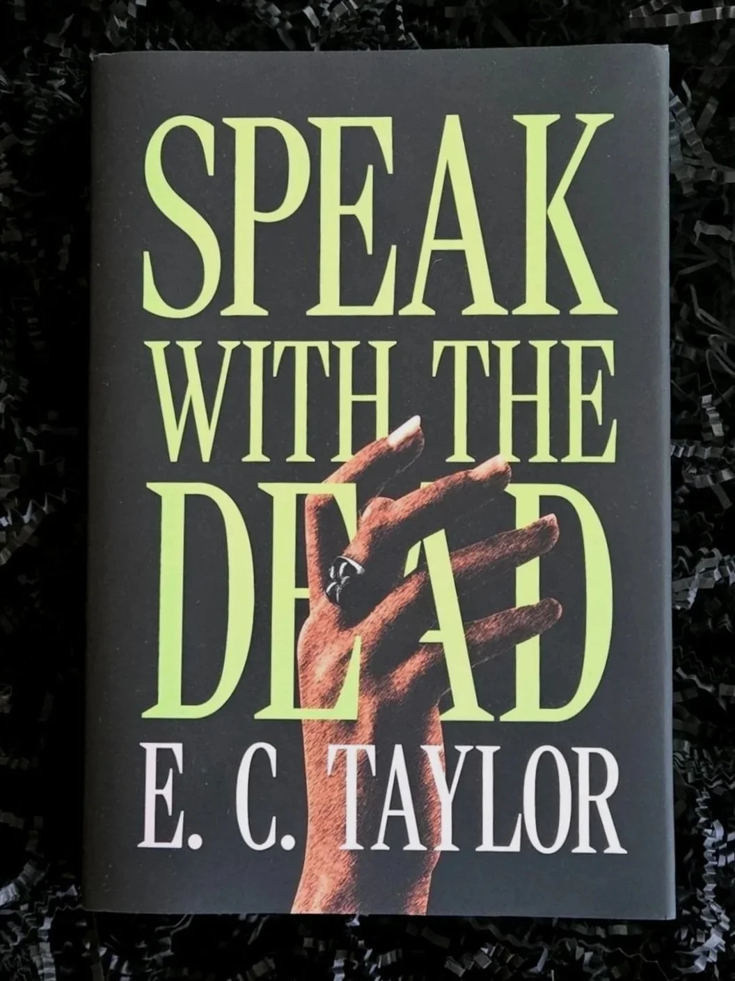 Book titled 'Speak with the Dead' by E. C. Taylor, featuring a hand holding a small object on the cover.