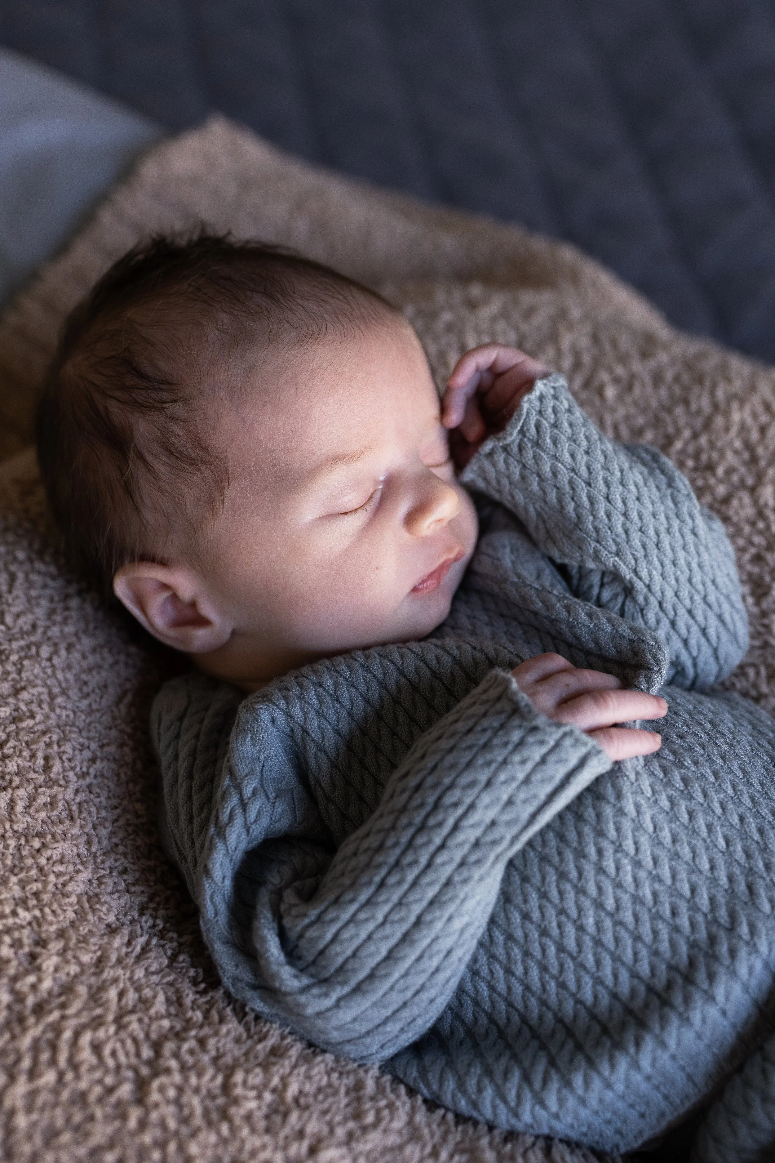 A sleeping baby lying on a soft, textured blanket, wearing a gray knit sweater.