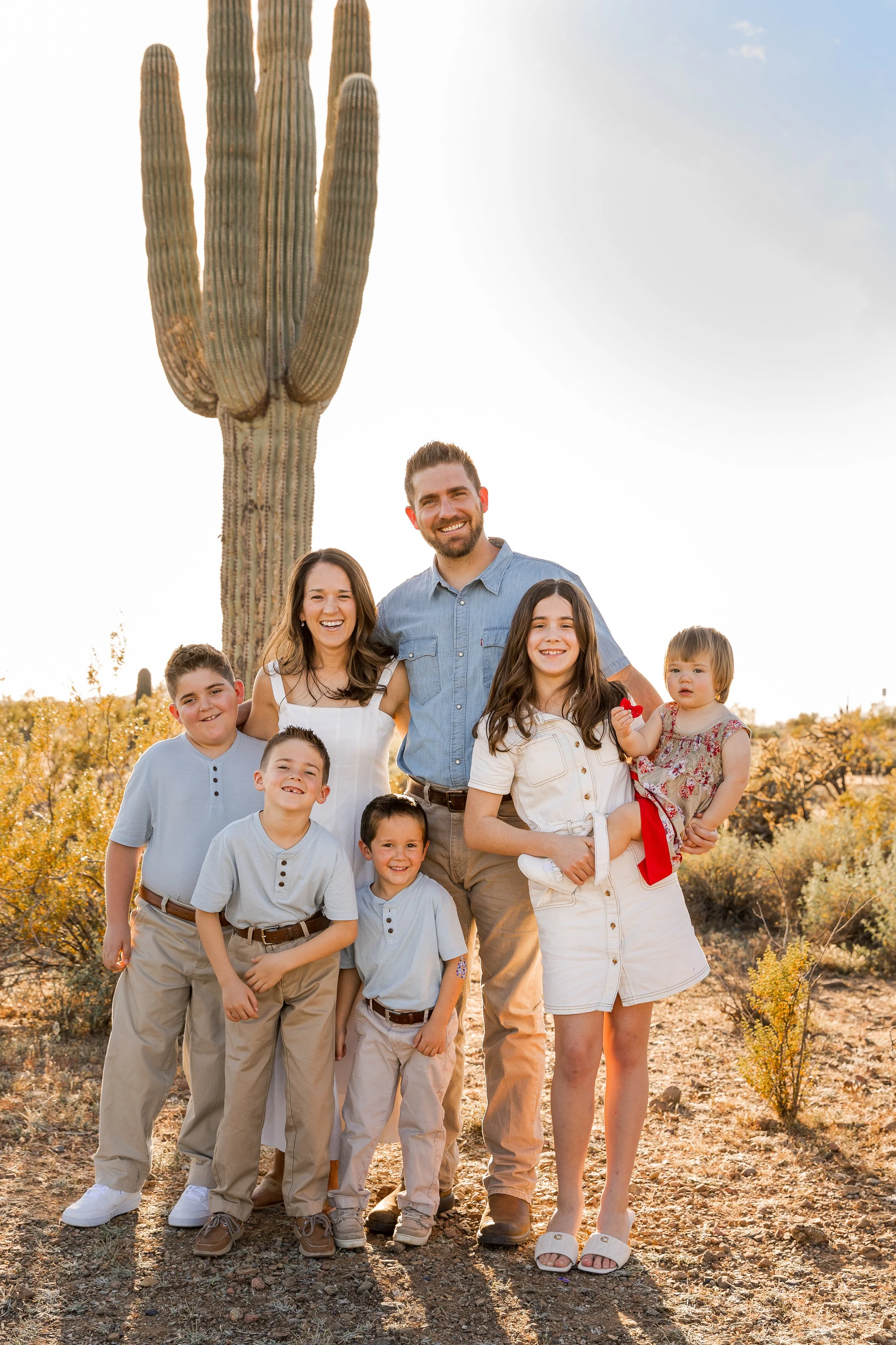 A group of children and a man smiling outdoors in a desert landscape with a large saguaro cactus in the background.