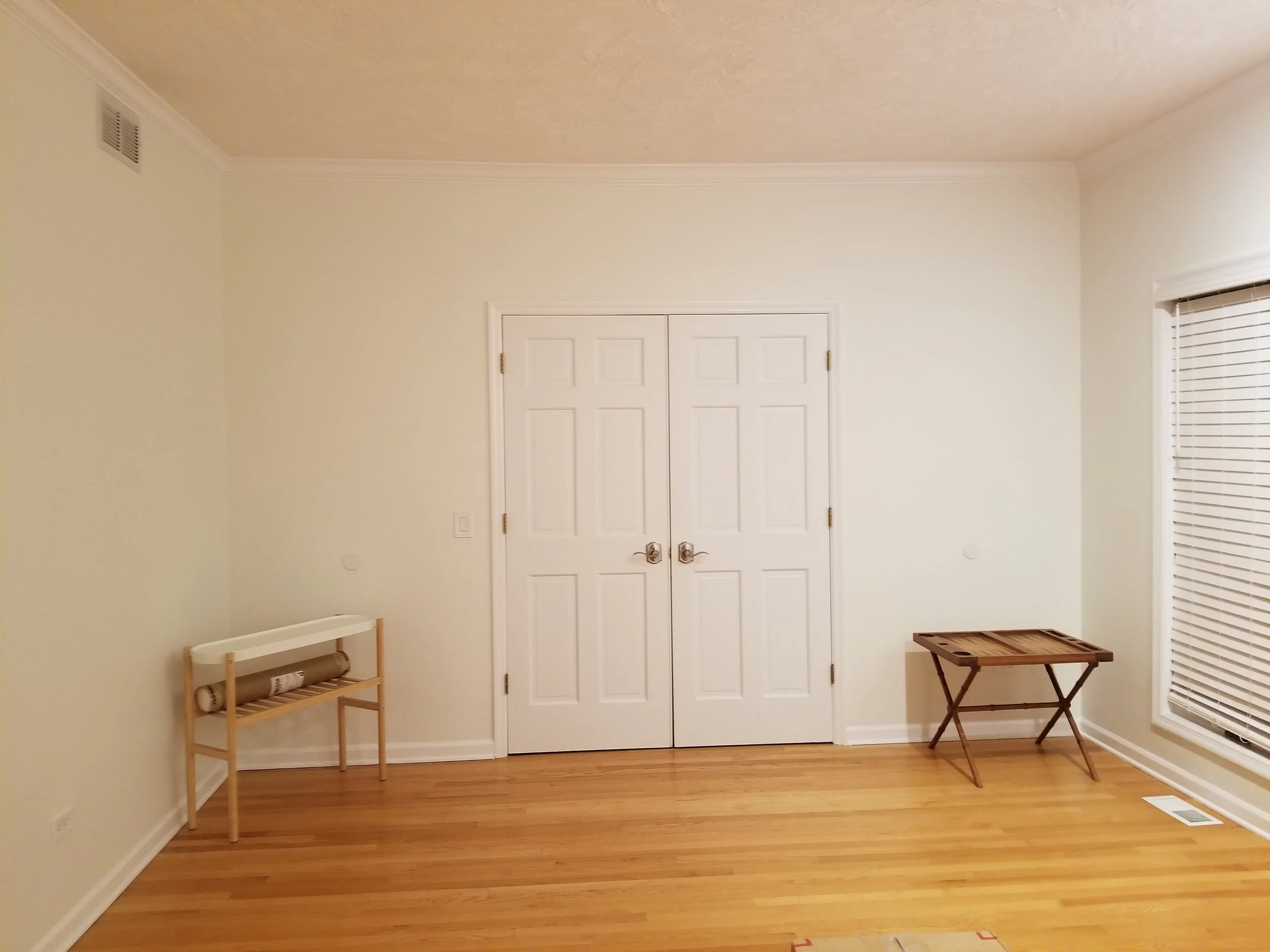 A simple yet professional example of a clean upper-level room. Features freshly painted off-white or light gray walls, crisp white double doors, and pristine baseboards. Shows professional quality on standard surfaces, with a glimpse of a natural lig