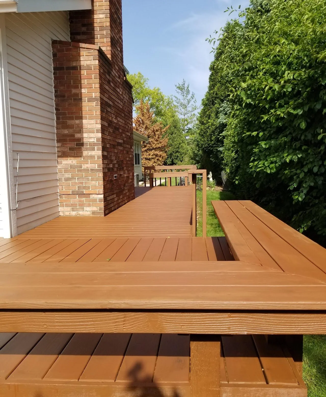 Professional wood deck restoration in Vernon Hills, IL. The image shows a multi-level cedar deck that has been stripped and finished with a rich brown solid stain, featuring clean lines along the built-in benches and brick chimney.