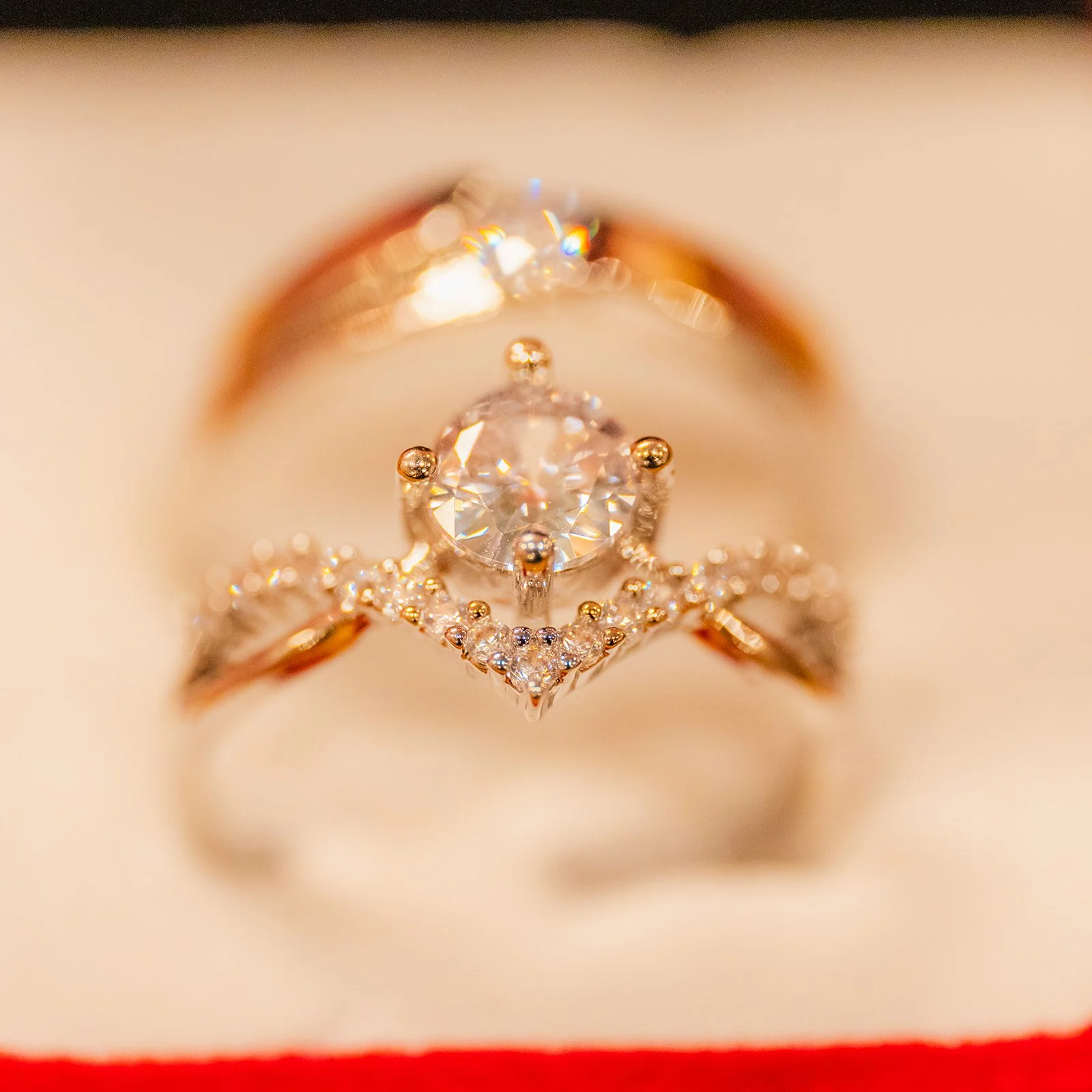 Close-up of a stack of three rings featuring a large central diamond in a prong setting, surrounded by smaller diamonds in a decorative design, on a soft beige background.
