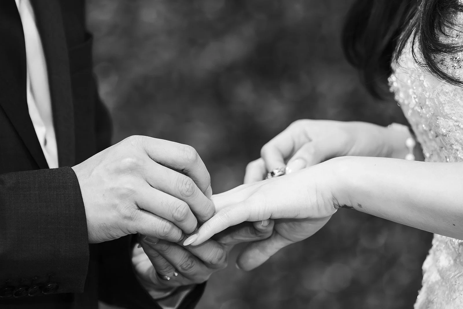 A man in a tuxedo holding the hand of a woman in a wedding dress, exchanging wedding rings.
