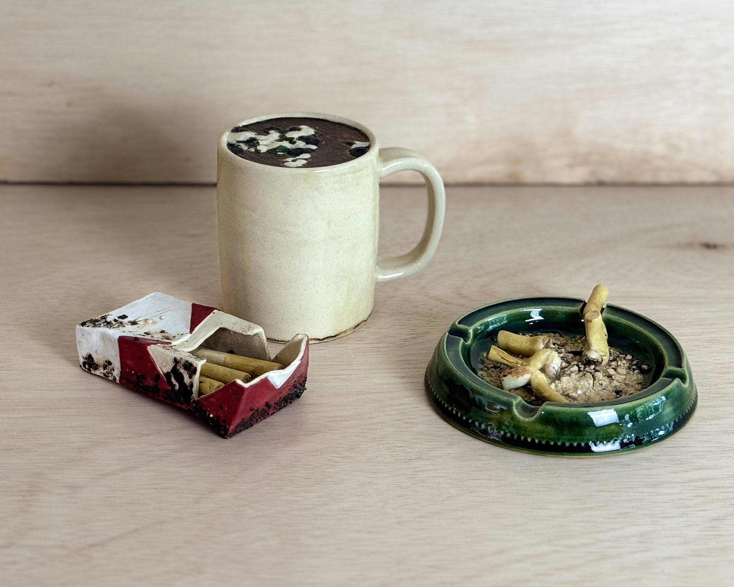 Ceramic sculpture of a moldy pack of cigarettes, coffee cup, and ash tray