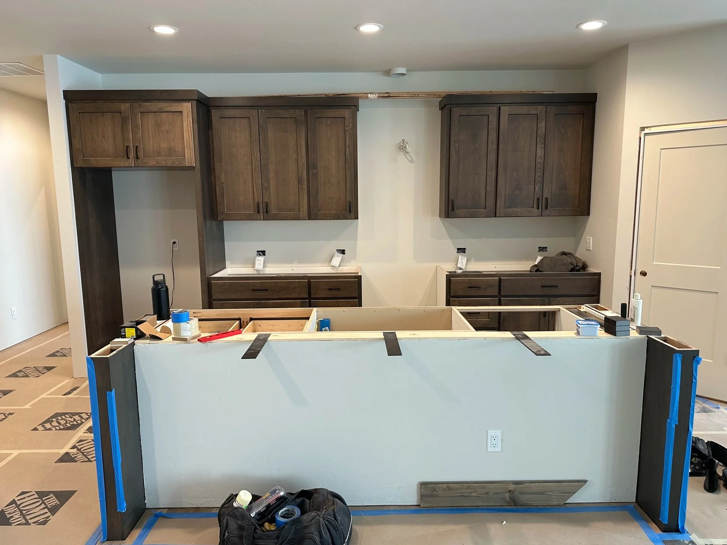 Kitchen under renovation with wooden cabinets, construction tools, and materials.