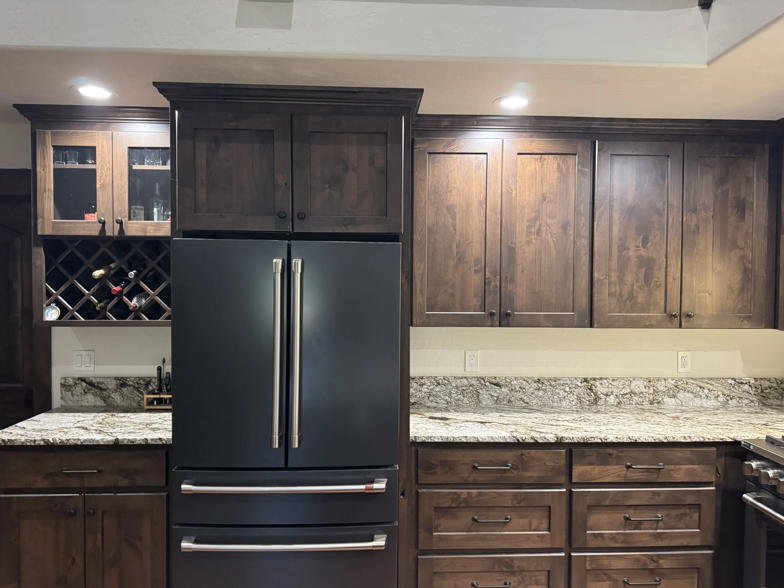 Kitchen with dark wood cabinets, granite countertop, and stainless steel refrigerator, with recessed lighting on ceiling.