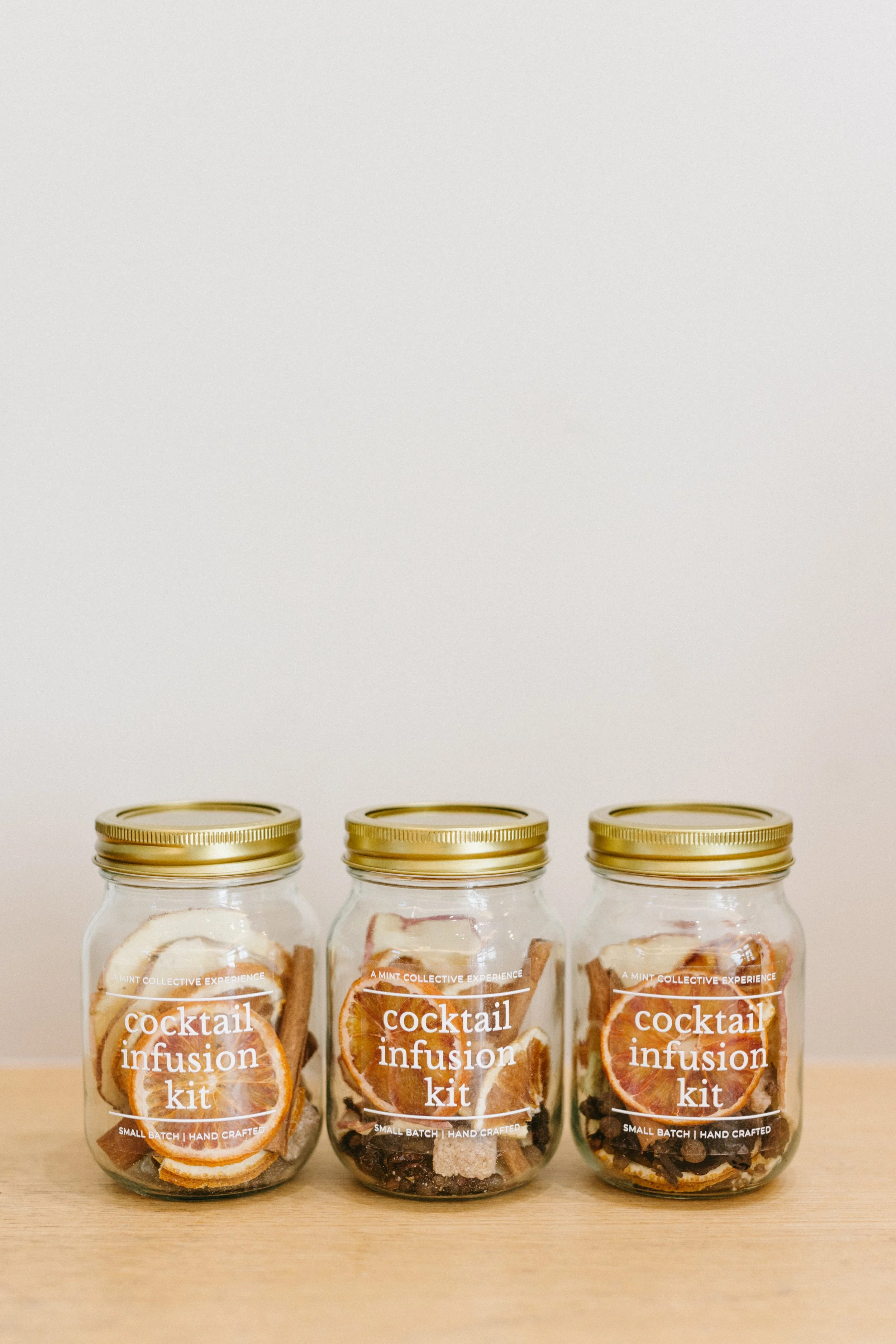 A lineup of artisanal Cocktail Infusion Kits, displaying a variety of dried orange slices, spices, and botanicals.