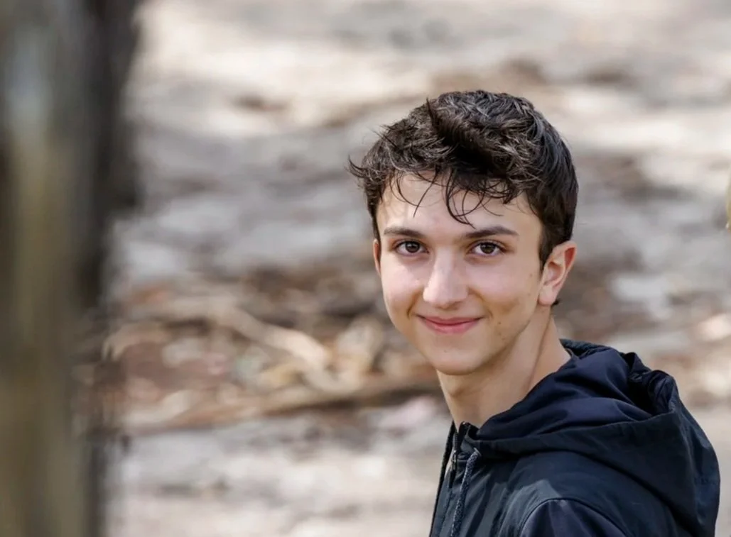 Young man with dark hair and a slight smile, outdoors in a natural setting with blurred background. William Stout, founder of The Will to Dance and director of the film The Will to Dance.