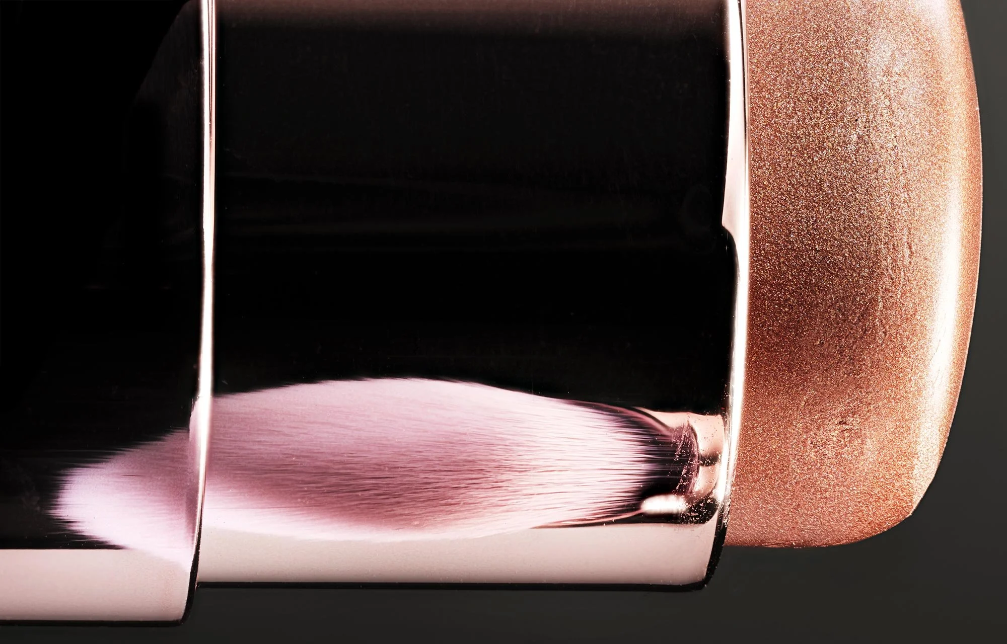Close-up of a metallic object with a reflective surface, a black section, and a textured, rose-gold colored part.