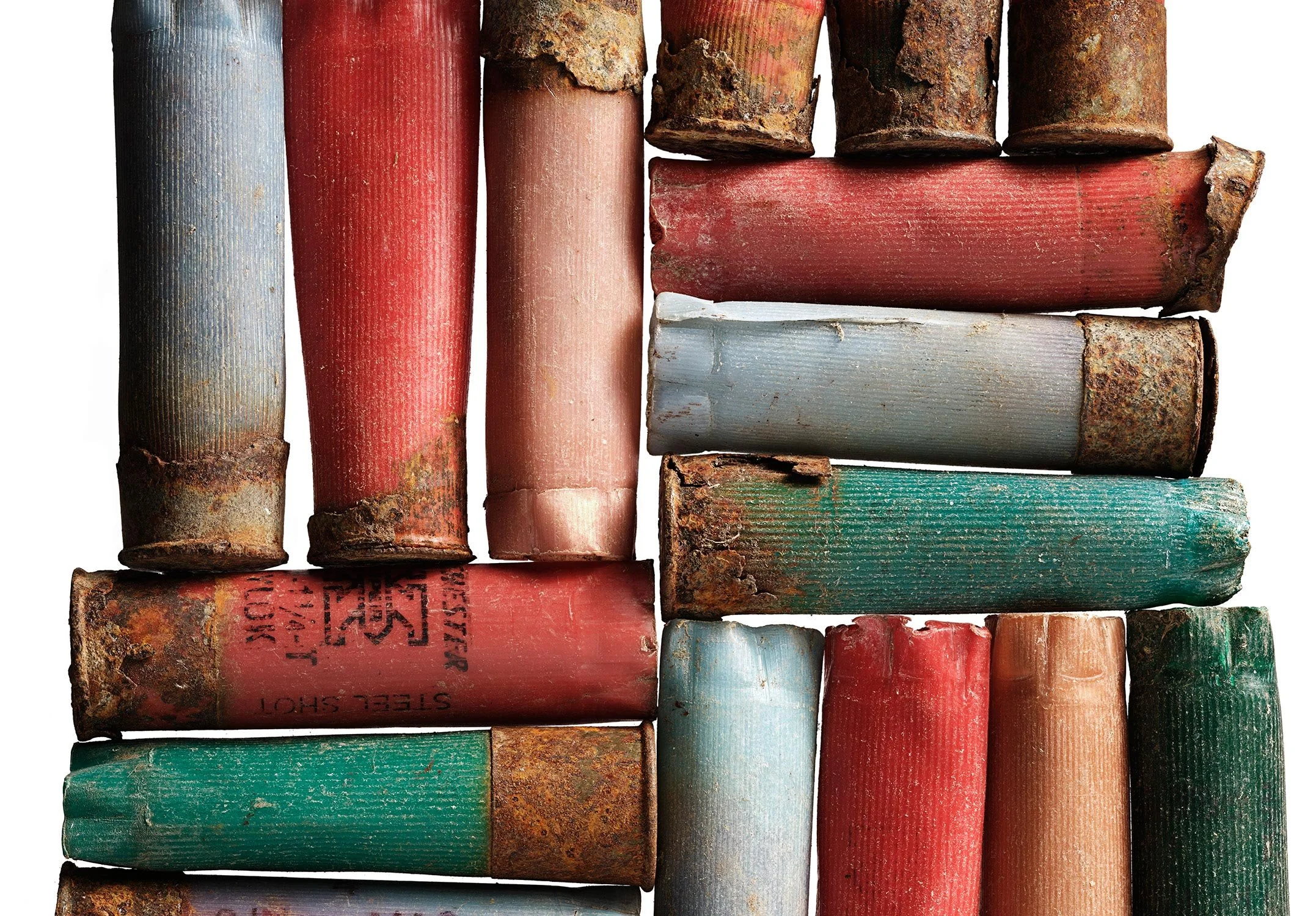 A collection of old, rusted shotgun shells arranged vertically and horizontally, showing chipped paint and corrosion.