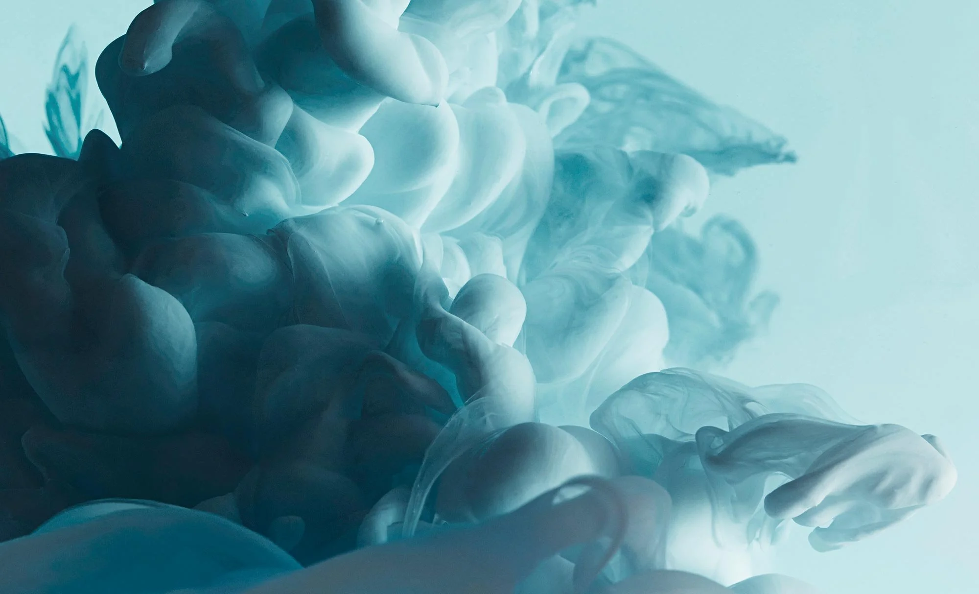 Swirling blue and white inks in water creating abstract cloud-like formations.