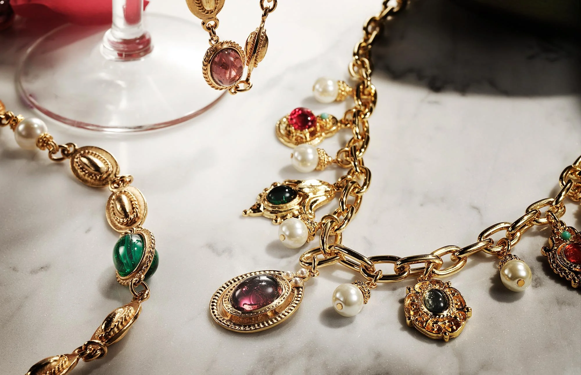 Gold jewelry with pearls and colorful gemstones on a white marble surface.