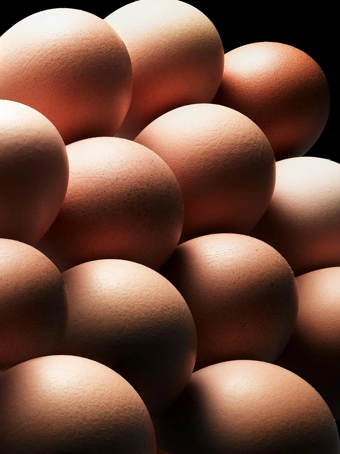 Close-up of multiple eggs stacked together, with a dark background highlighting their texture and shape.