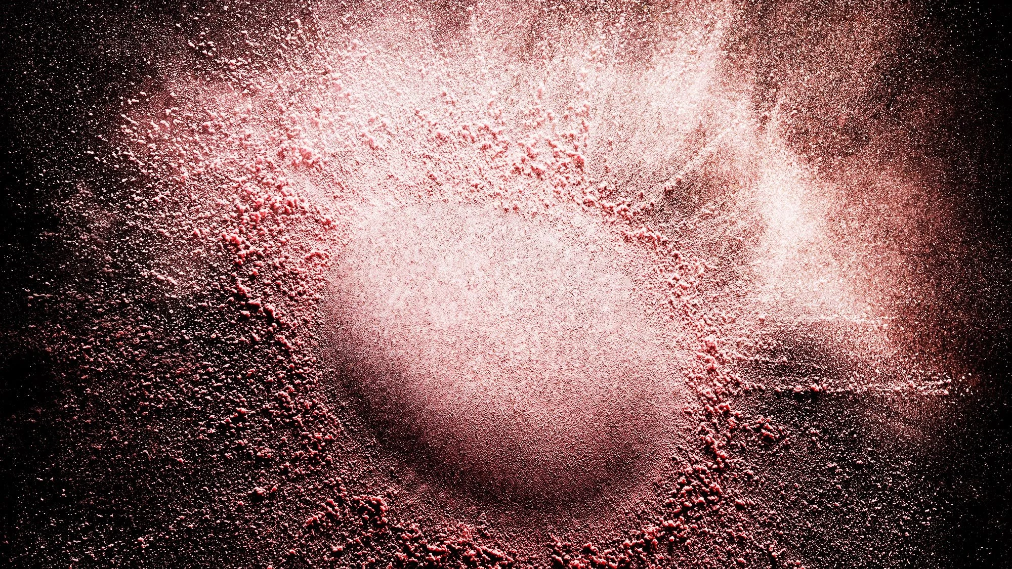 Still life cosmetic photography capturing powder in motion with controlled lighting.