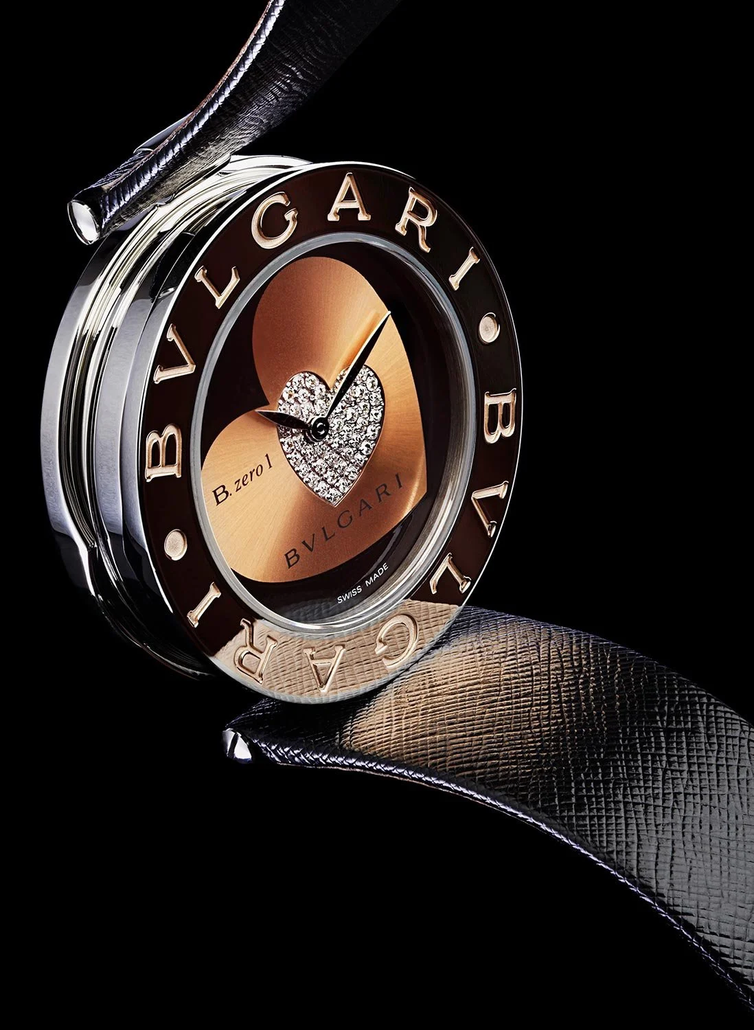 Close-up of a luxury Bulgari wristwatch with a black strap, round silver bezel, and bronze and diamond heart design on the dial.