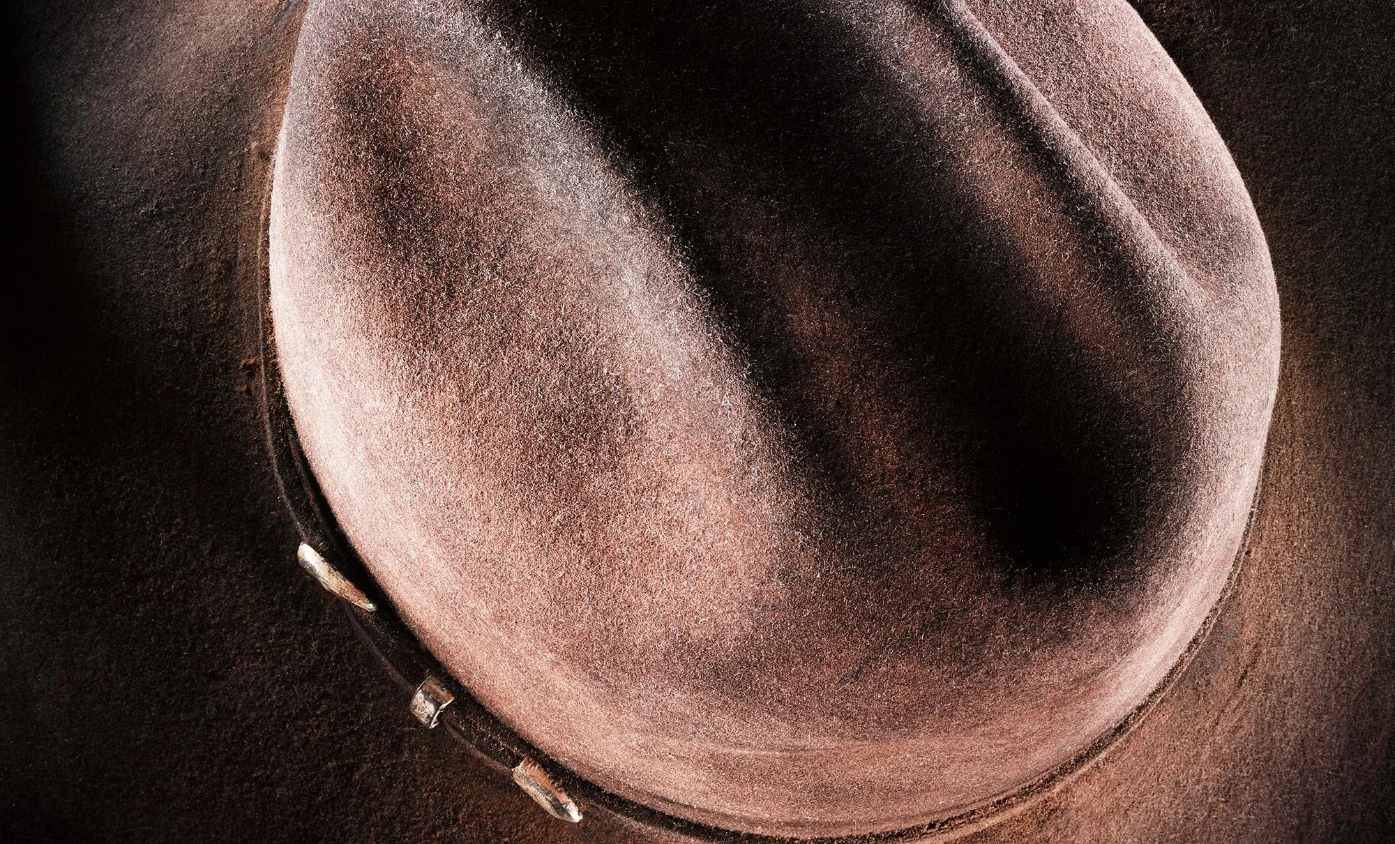 A close-up view of a brown cowboy hat with a black band and metallic accents.
