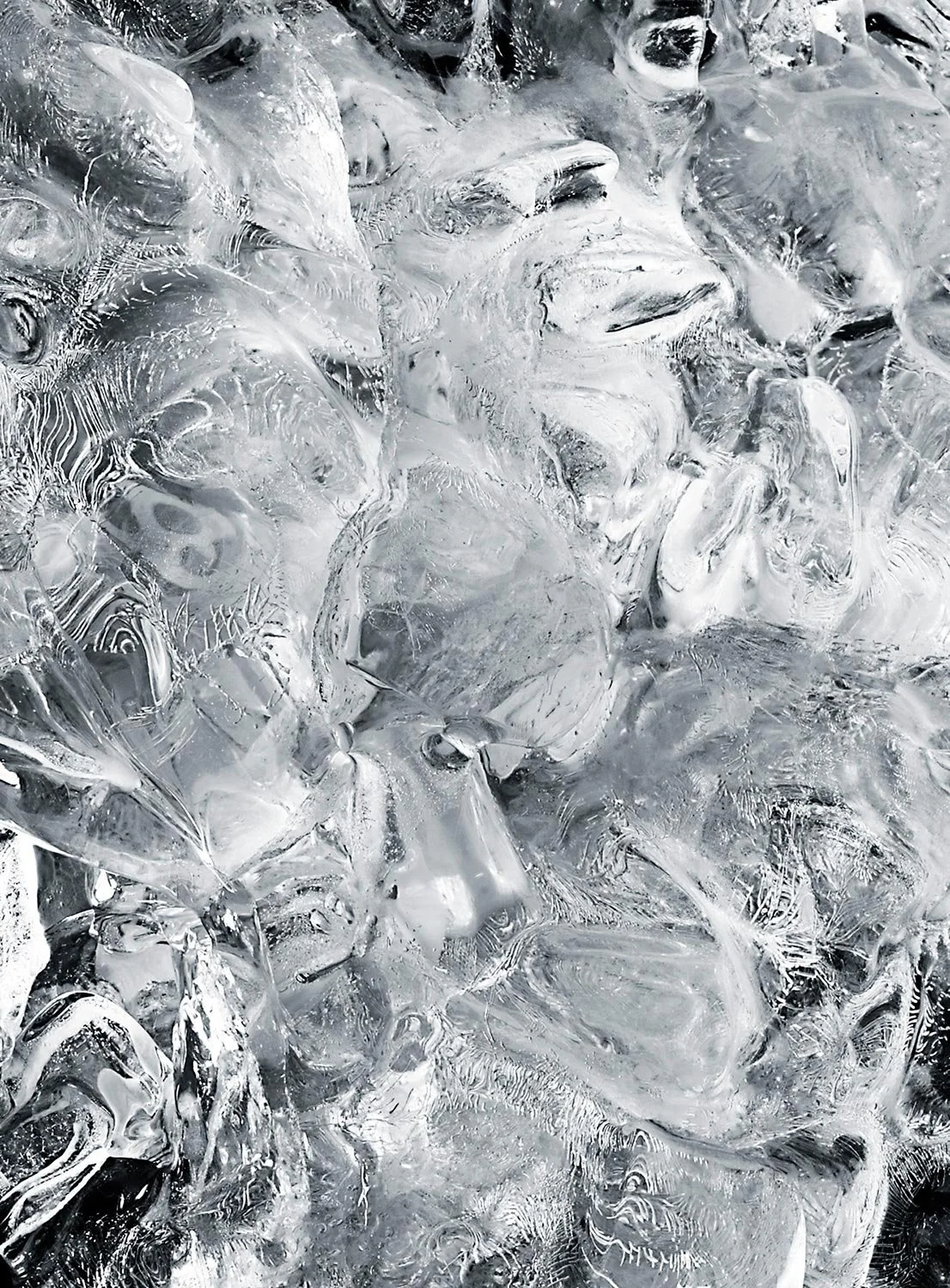 Close-up of a pile of irregularly shaped, clear ice cubes with light reflections.