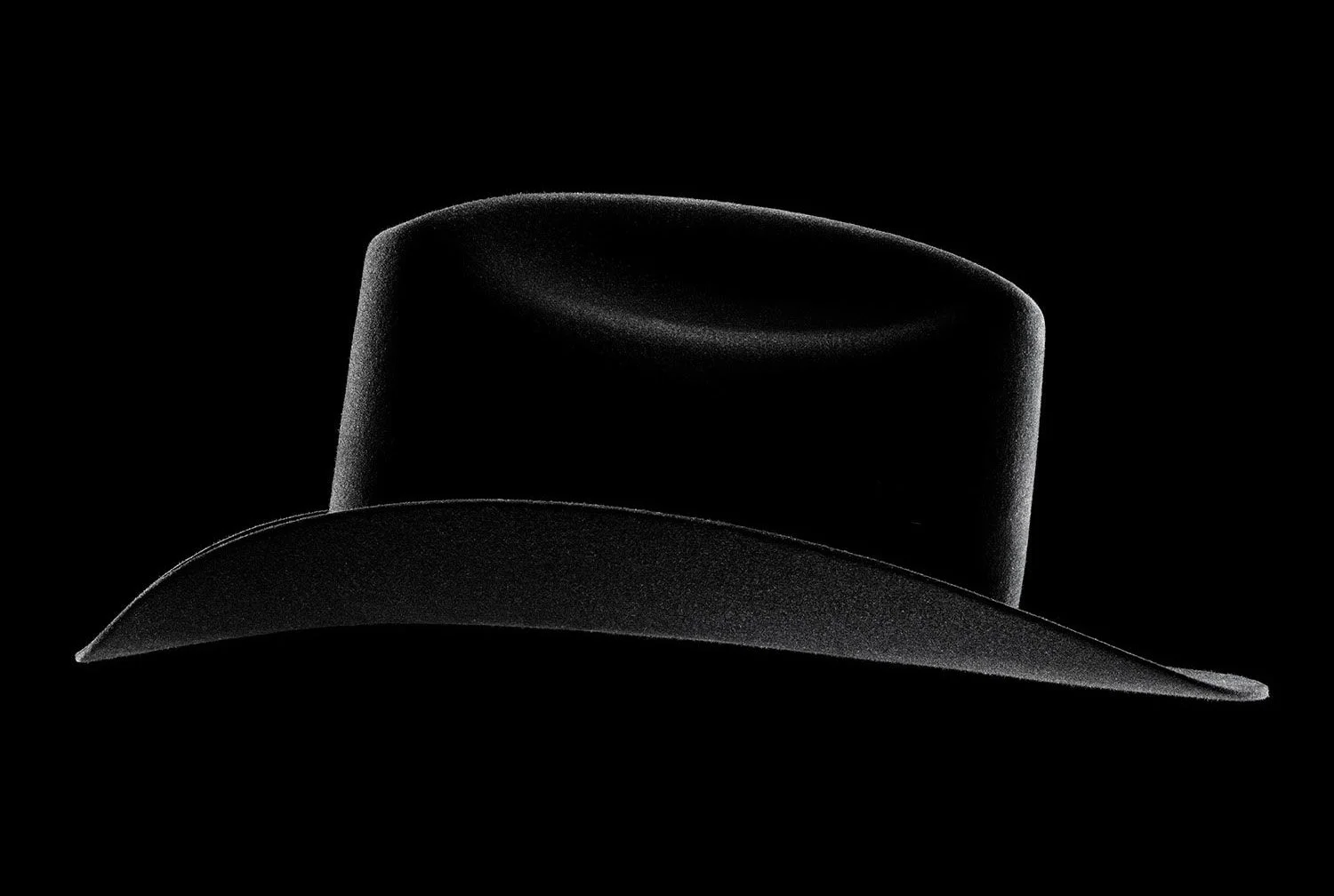 A black cowboy hat with a wide brim, photographed against a black background, with a matte finish.