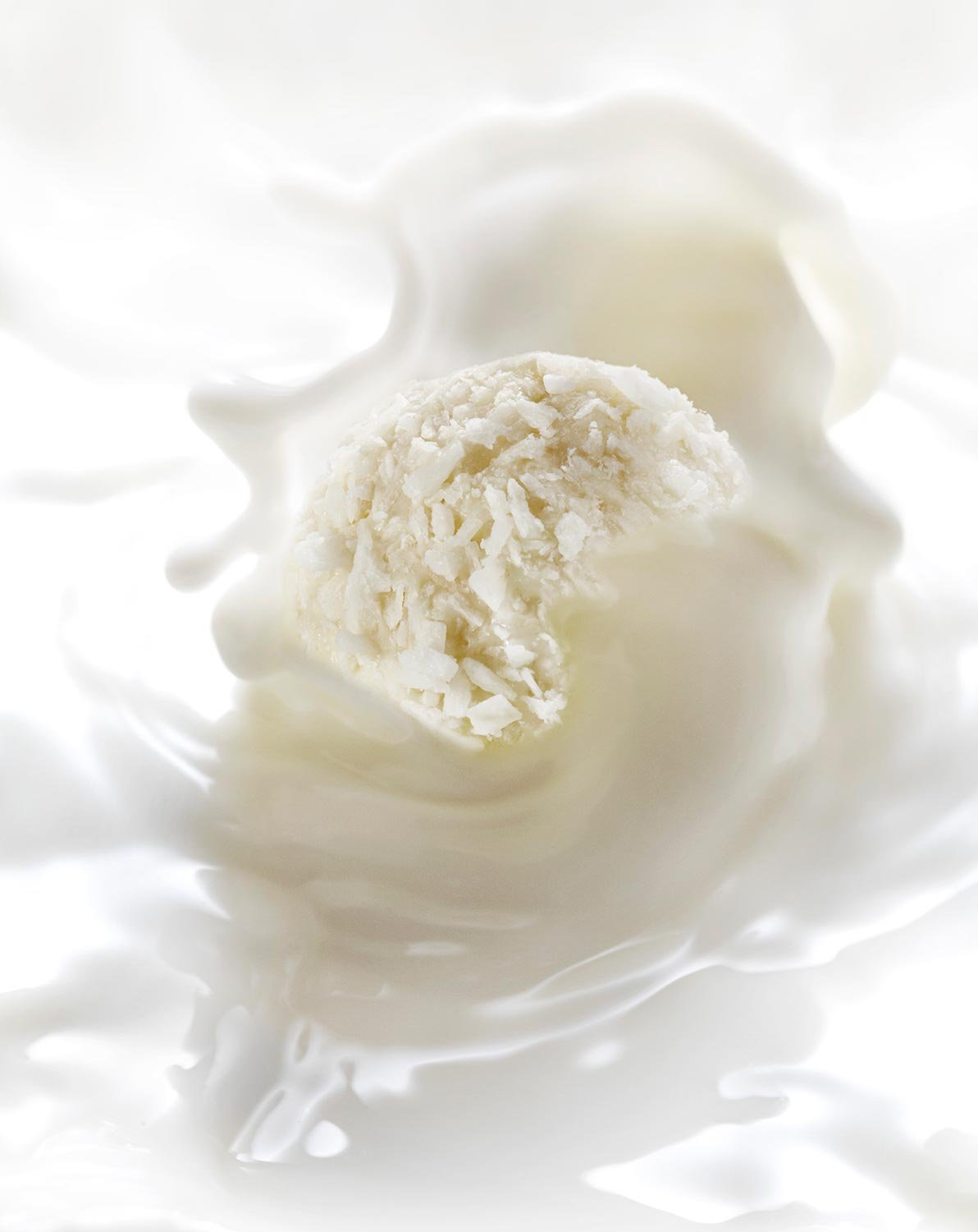 A white chocolate truffle being dipped into white chocolate.