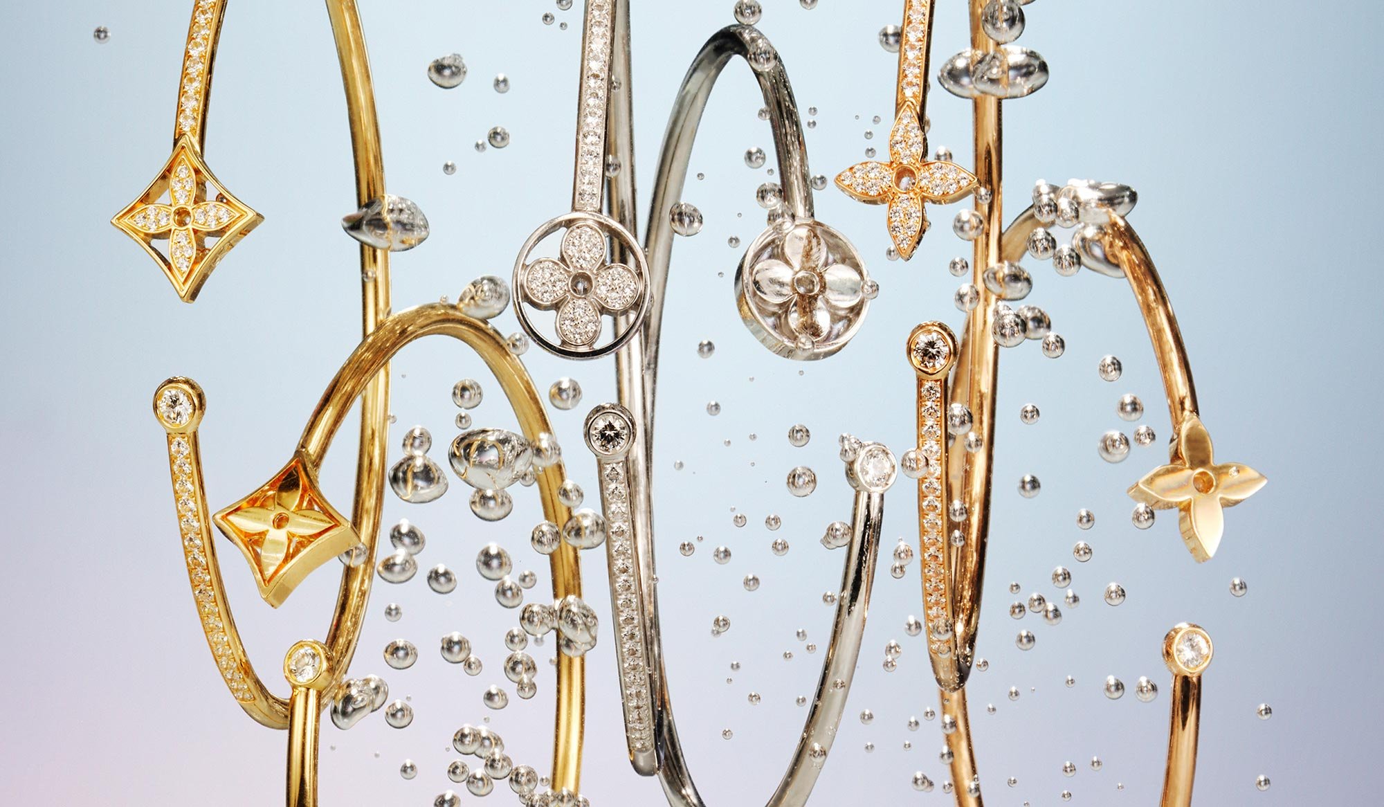 Various gold and silver jewelry bracelets and bangles decorated with diamonds and floral motifs, suspended against a light background.