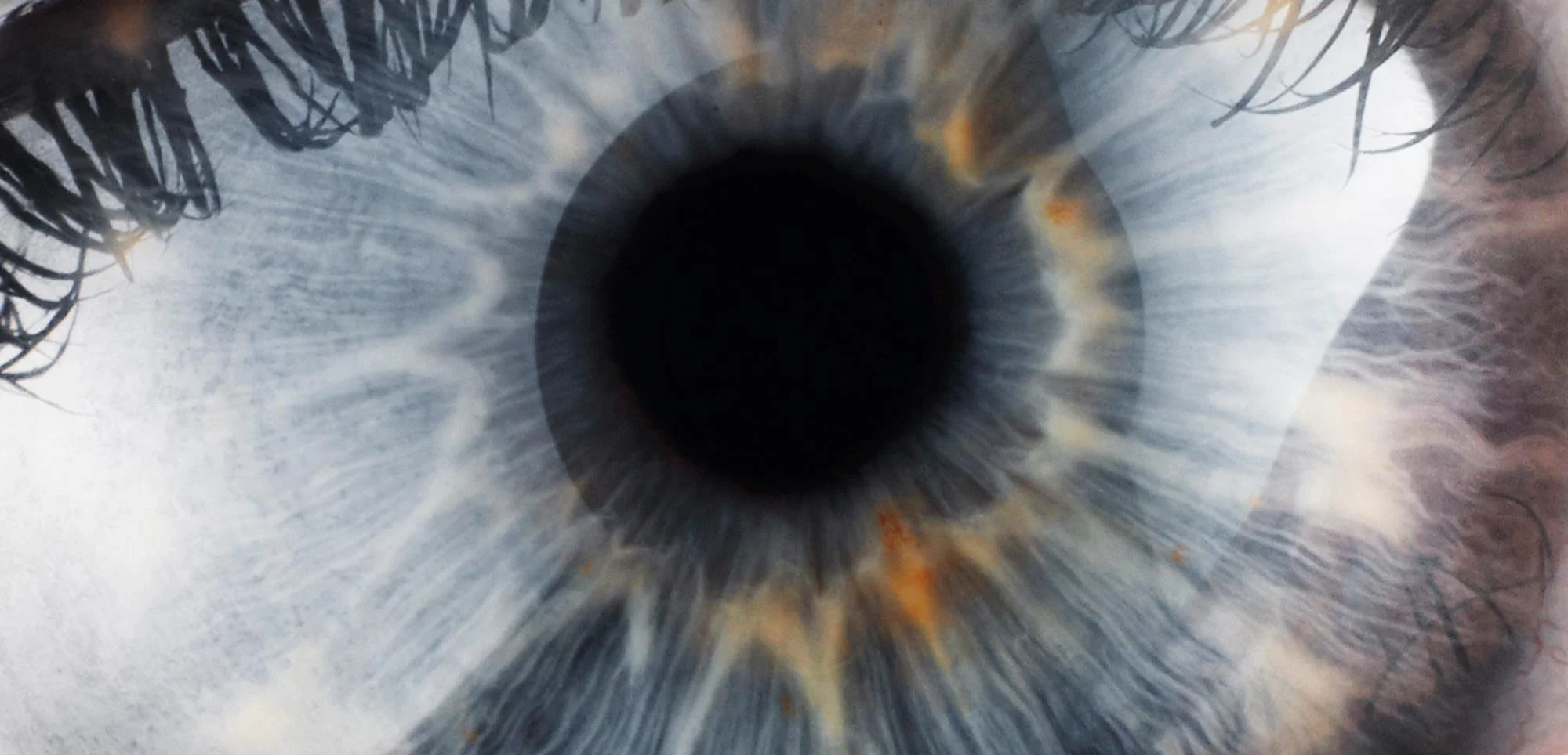 Close-up of a human eye revealing the iris with intricate blue and grey patterns surrounding a dark pupil.