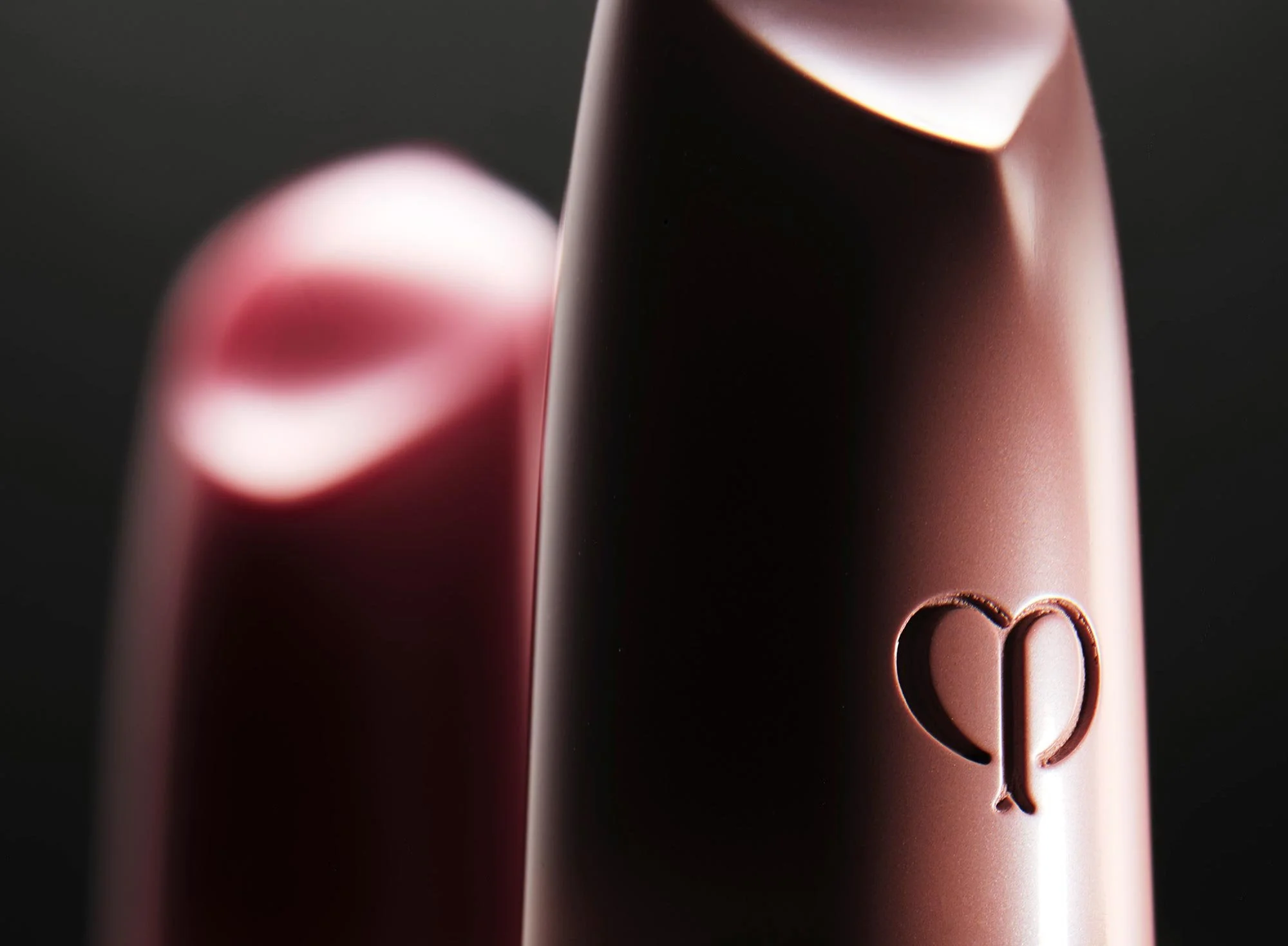 Close-up of two lipstick tubes, one in the foreground with a heart-shaped engraving, and one in the background, both with a matte finish.